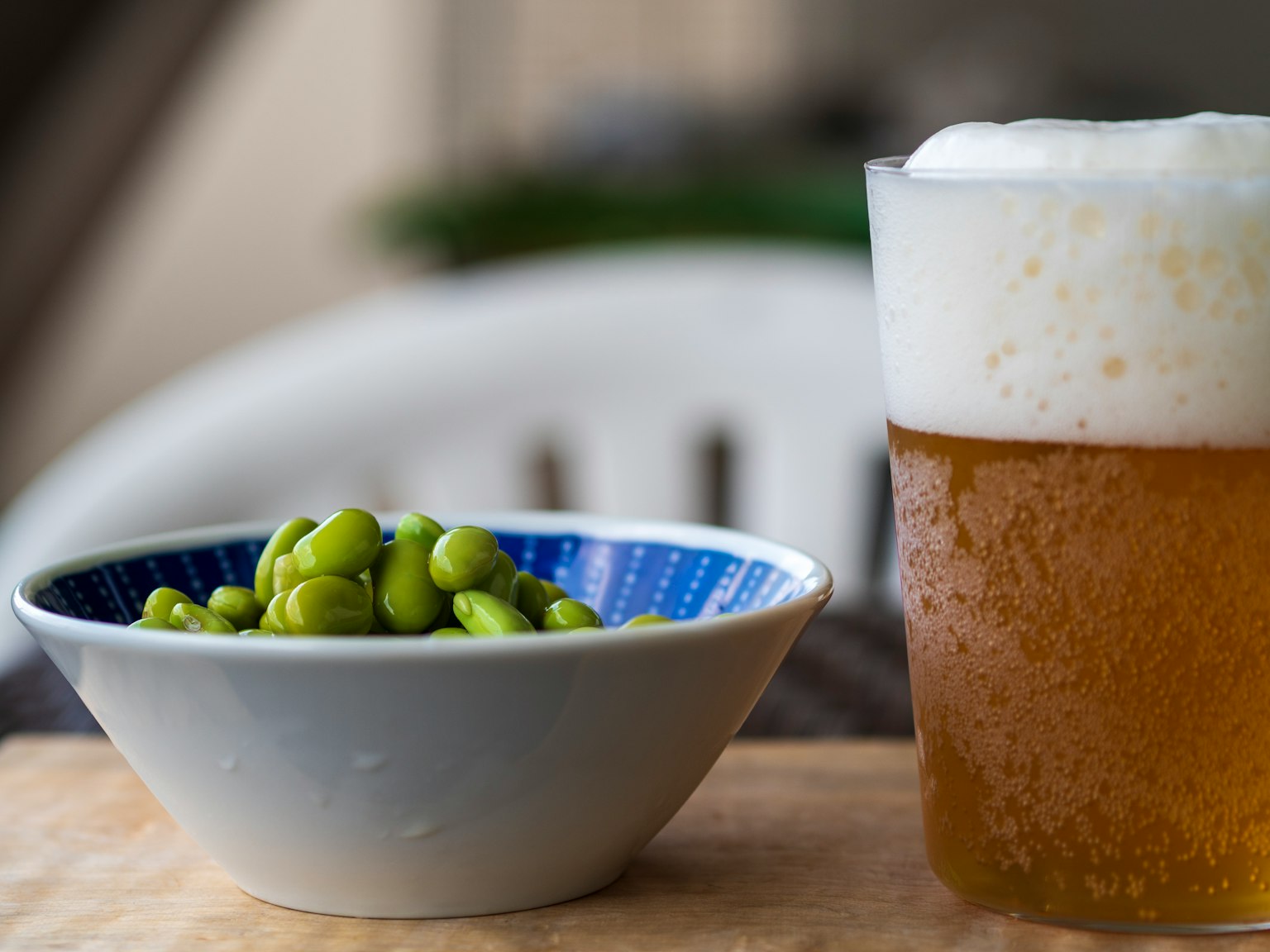 Foto di birra e edamame La birra è di un colore dorato e schiumoso L'edamame è servito in una ciotola blu