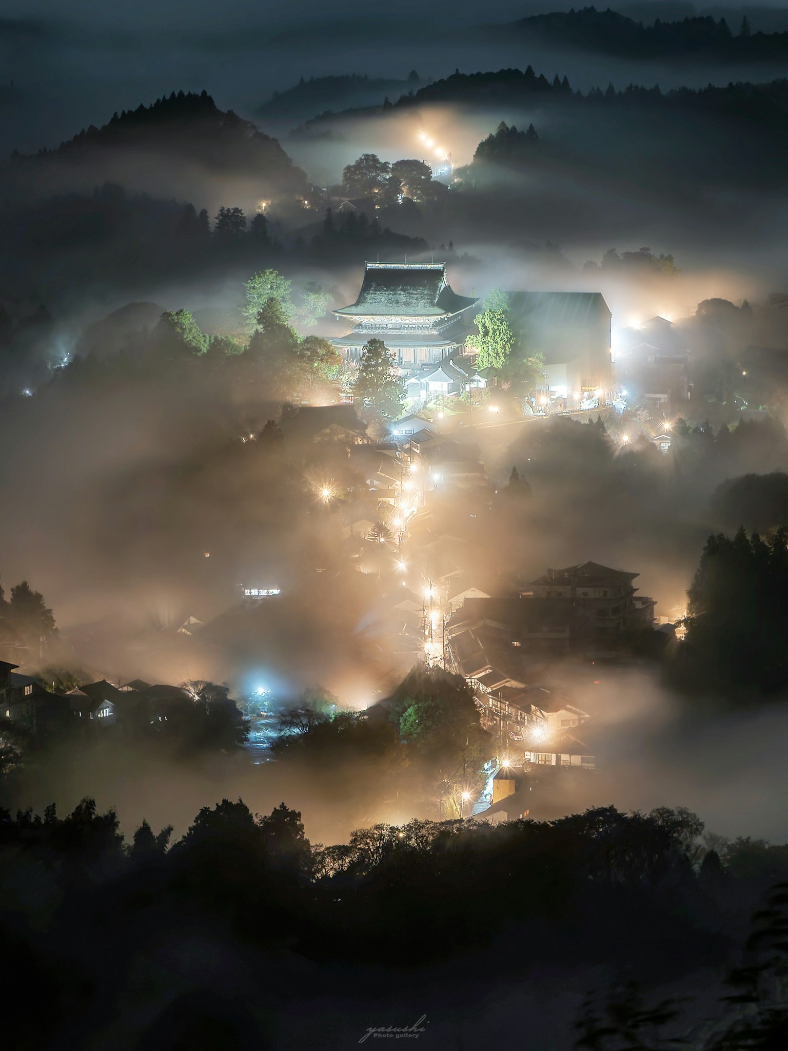 霧に包まれた山々の中にある美しい寺院の夜景 明かりが点在し幻想的な雰囲気を醸し出す