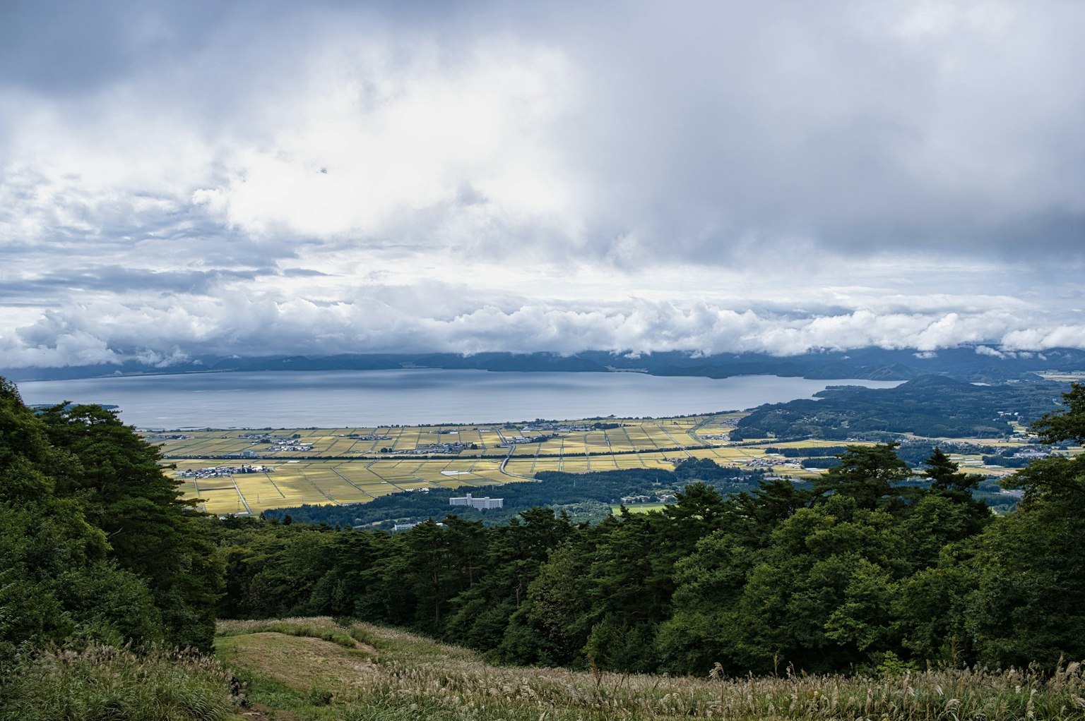 Panoramablick auf einen See umgeben von grünen Hügeln und Wolken