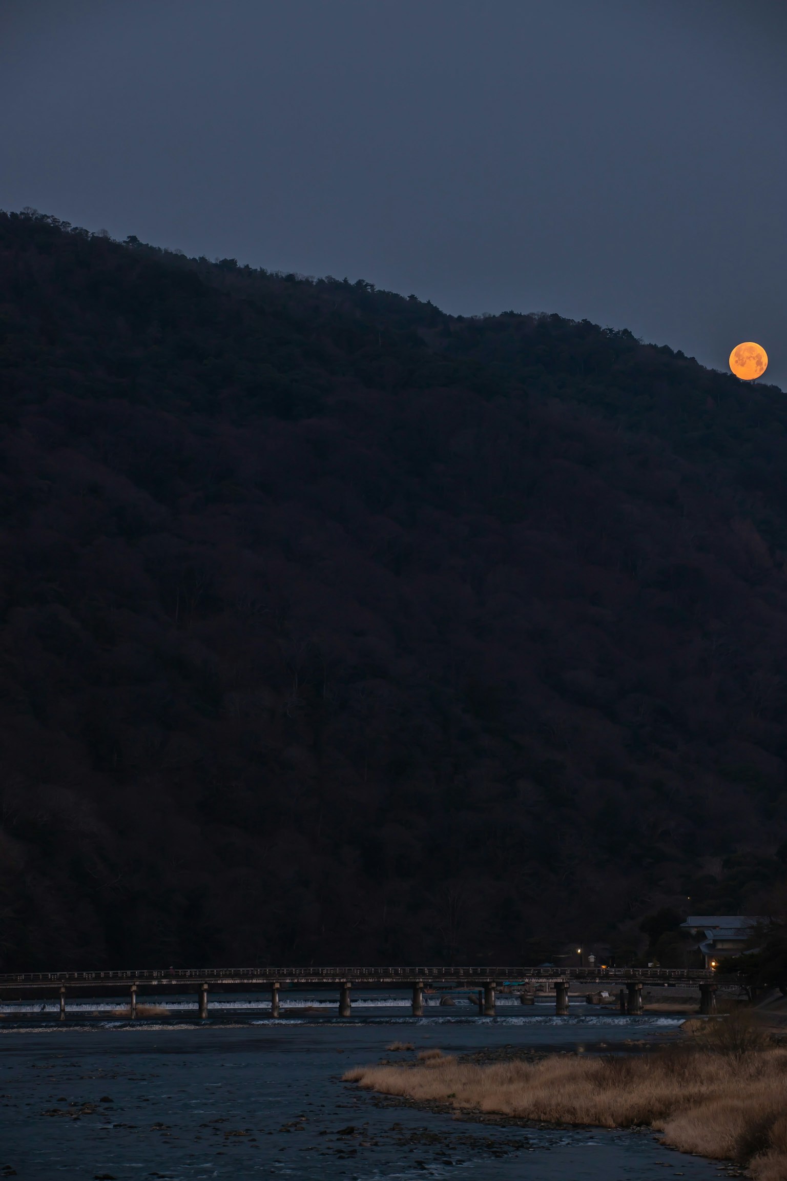 Vue pittoresque d'une rivière avec un pont et une grande lune se levant sur les montagnes