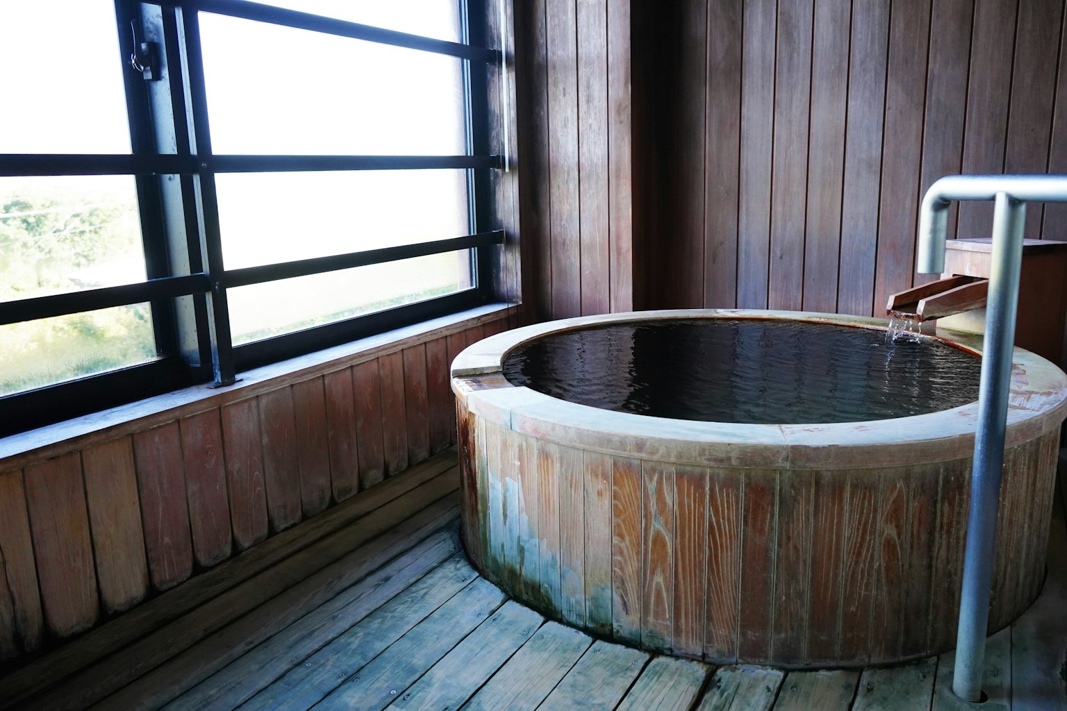 Bain thermal intérieur avec une baignoire en bois et de grandes fenêtres