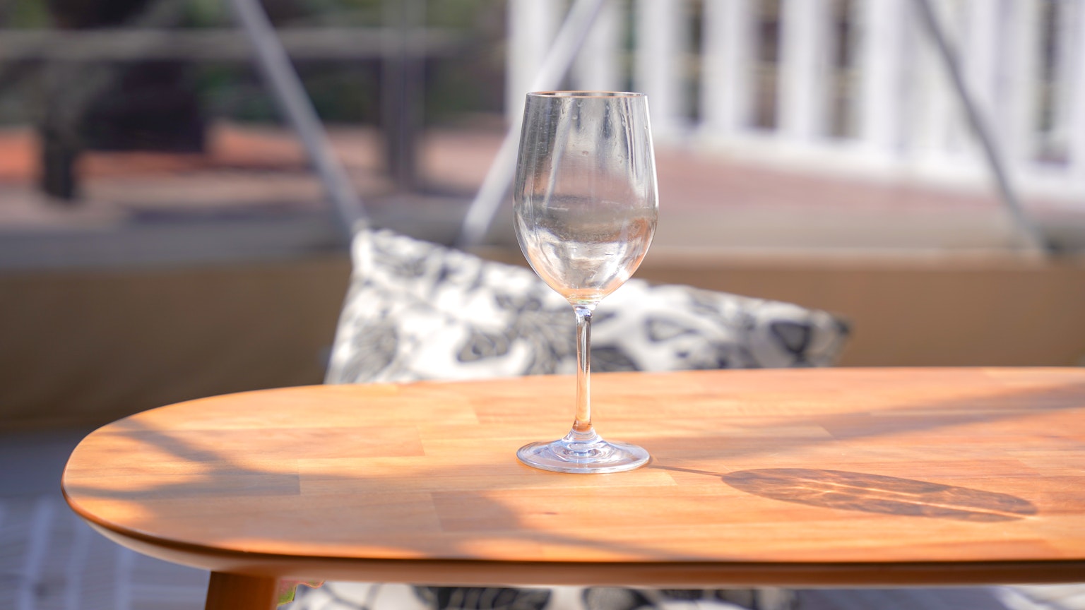 Un bicchiere di vino trasparente posato su un tavolo di legno con un cuscino decorativo sullo sfondo