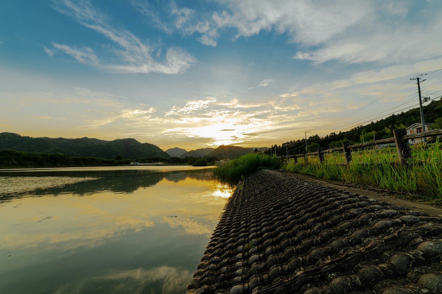 Pemandangan indah matahari terbenam di atas danau tenang dengan pegunungan di latar belakang