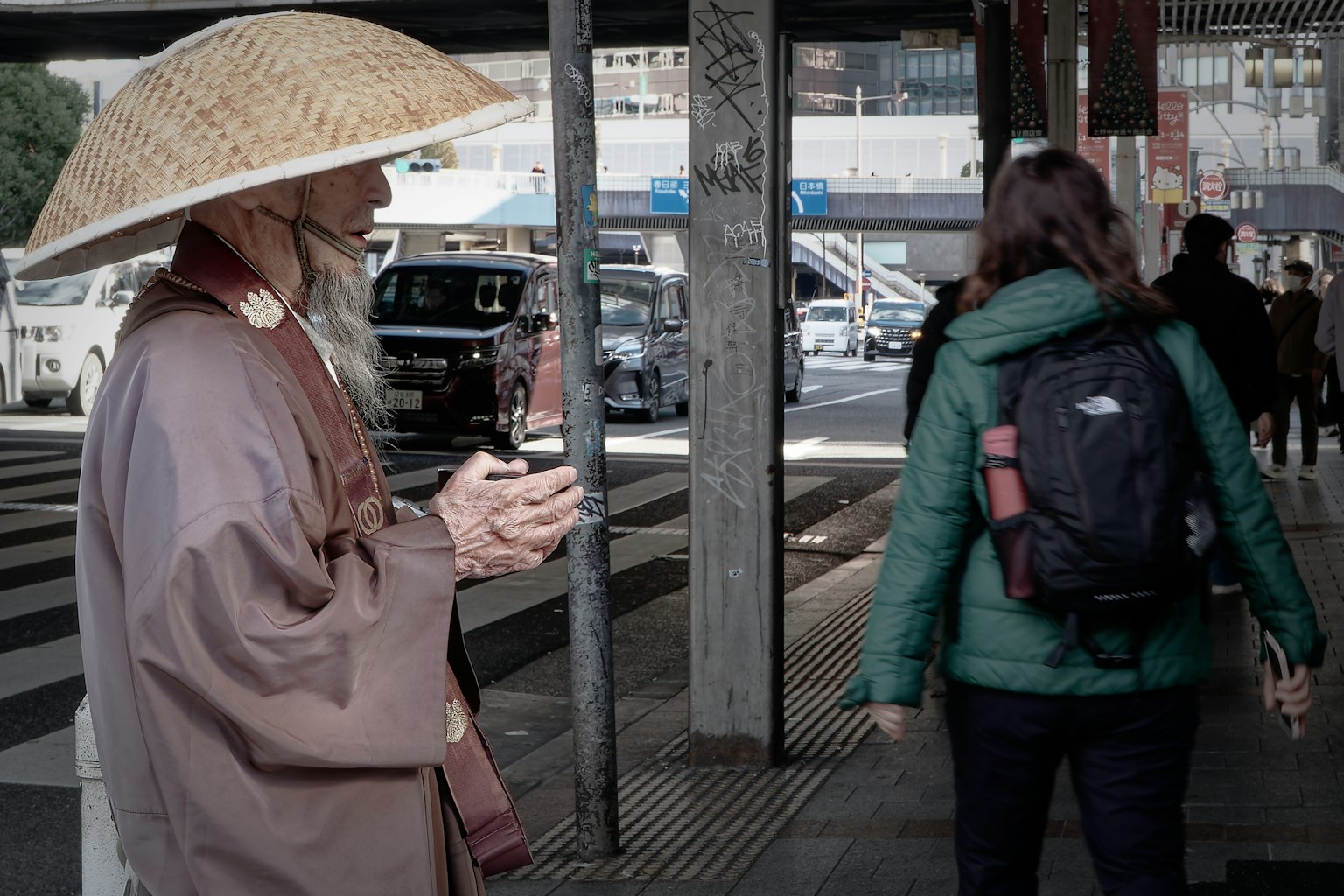 Un hombre mayor con vestimenta tradicional y sombrero de paja está de pie en la acera
