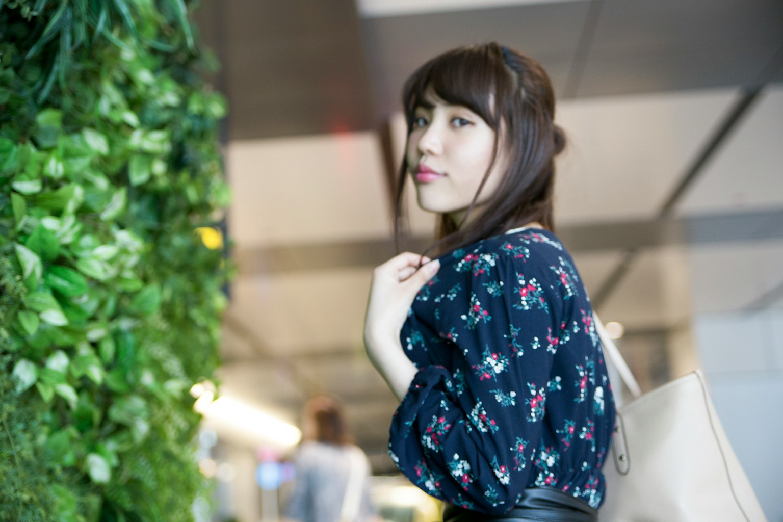 Portrait of a woman standing near a green wall wearing a floral blouse