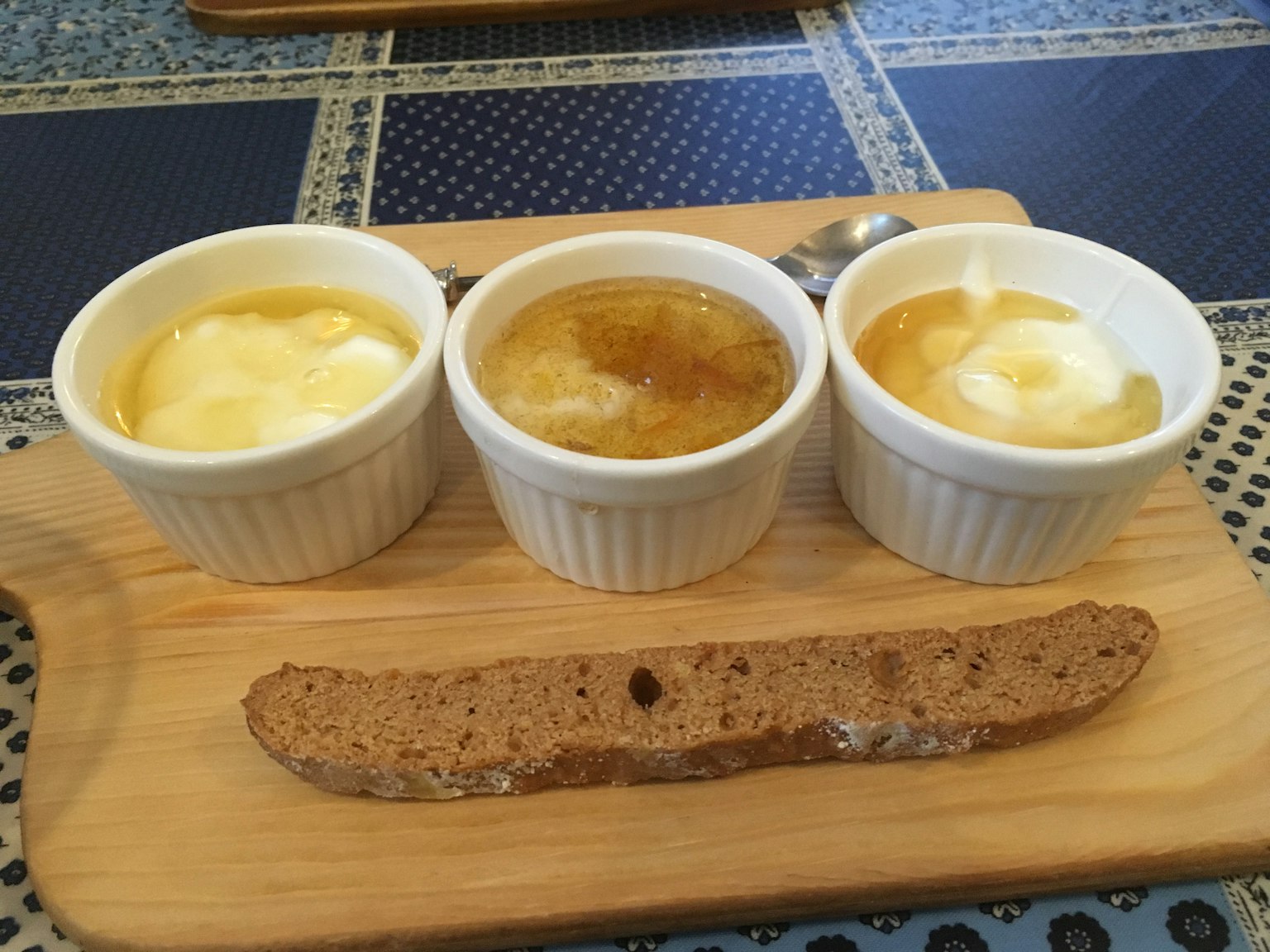 Tres pequeñas tazas blancas llenas de postres sobre una tabla de madera con una galleta