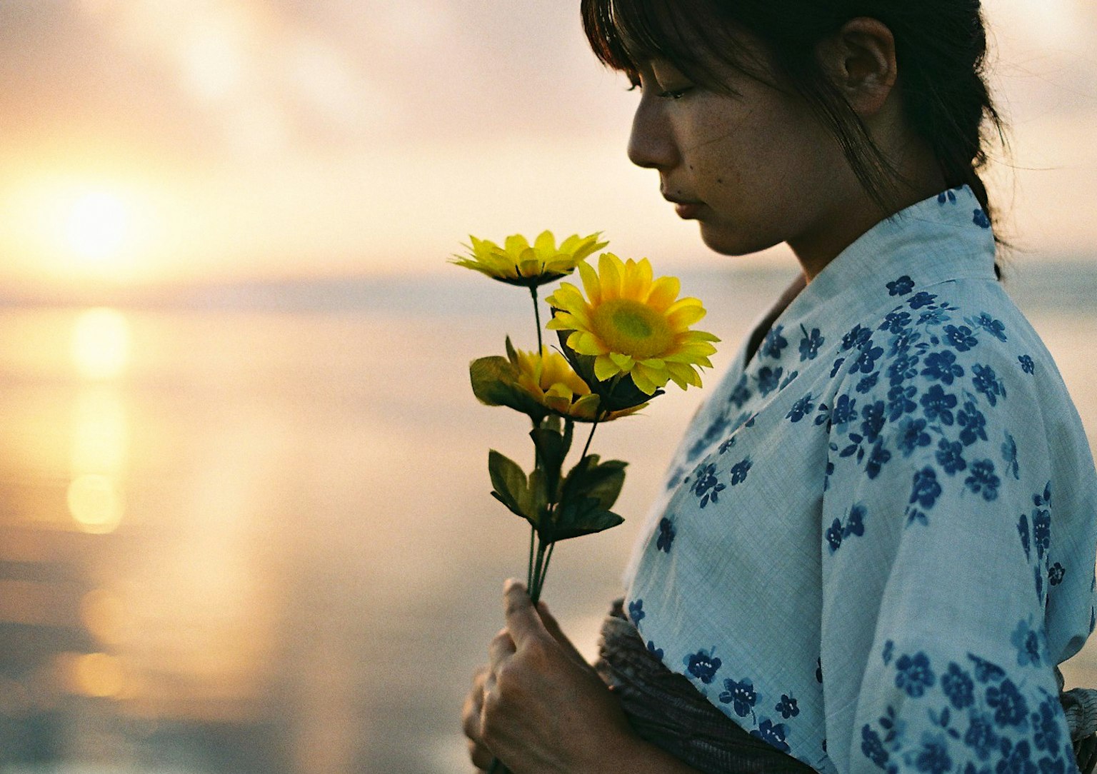 Une femme en tenue traditionnelle tenant des tournesols sur fond de coucher de soleil