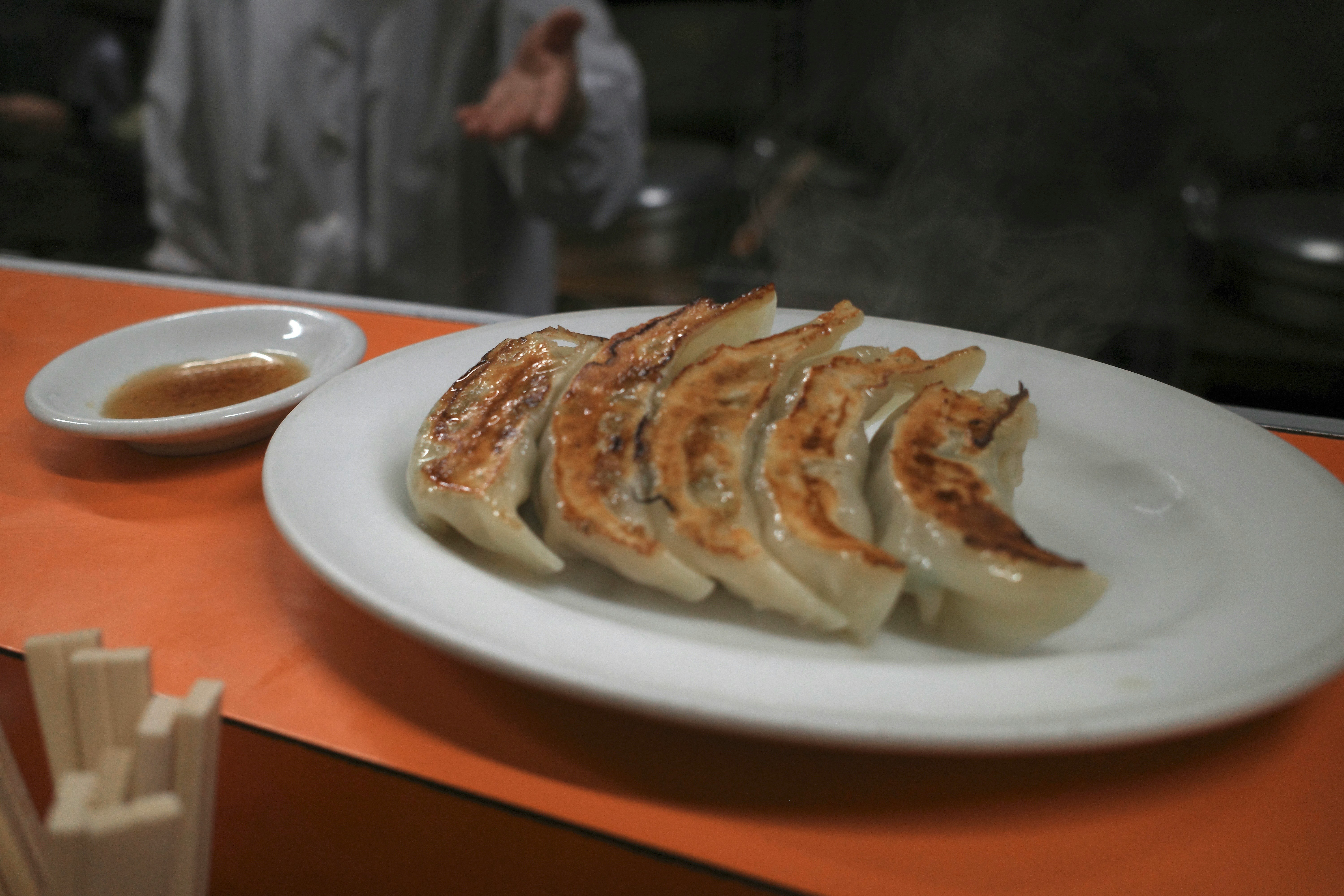 オレンジ色のテーブルに並ぶ焼き餃子とスープの皿