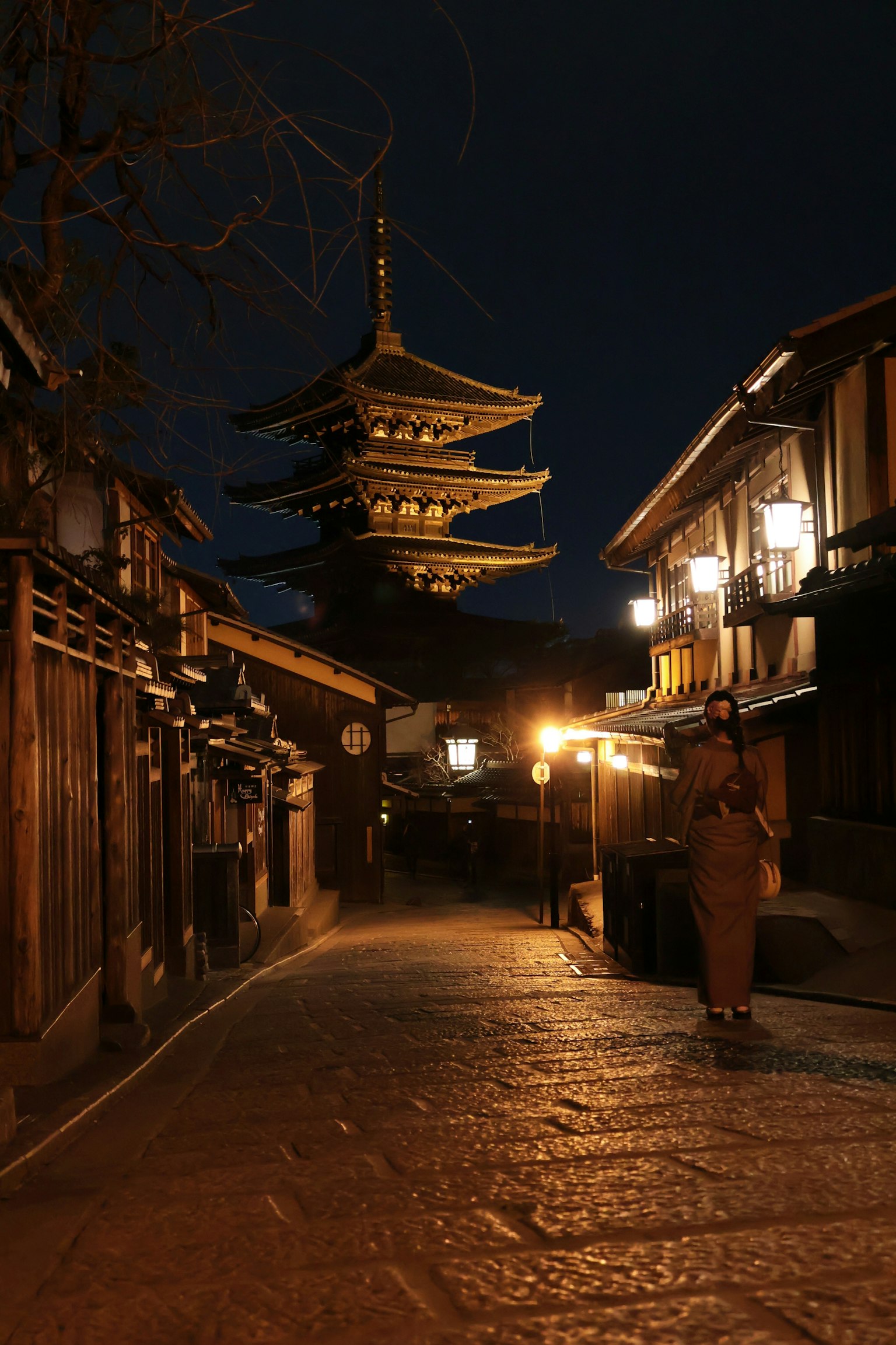 Une femme en vêtements traditionnels marchant sur une rue pavée avec une pagode en arrière-plan la nuit