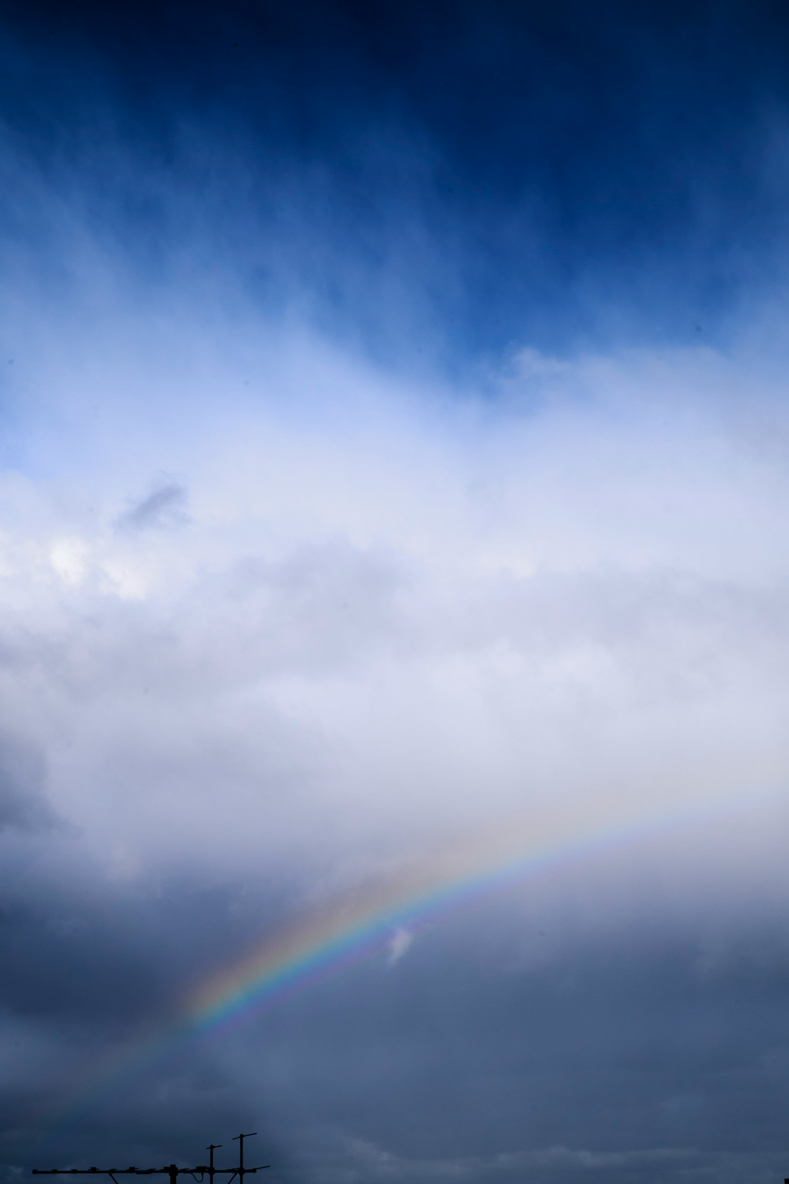 Ein Regenbogen, der zwischen blauen Himmel und Wolken aufspannt