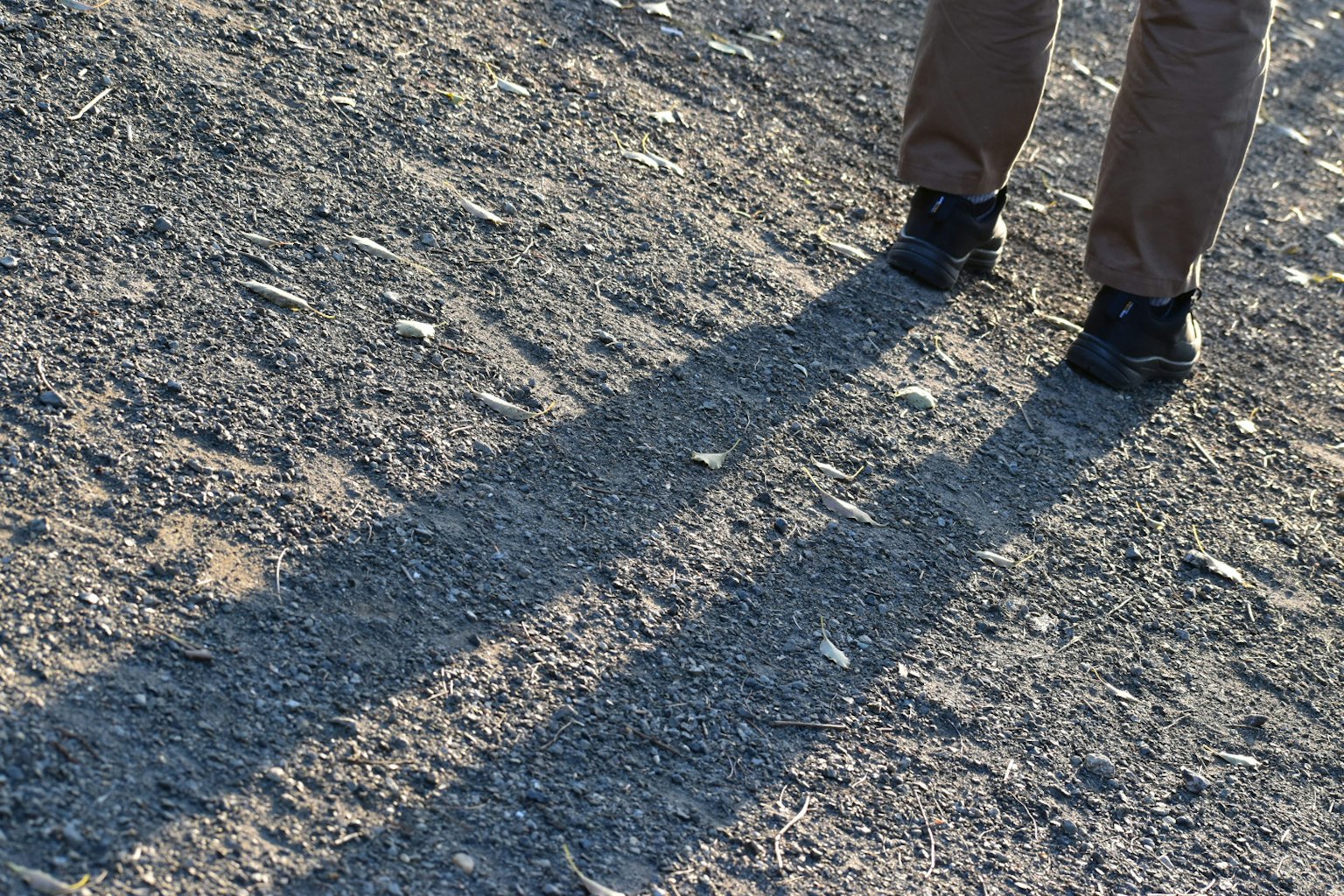 Foto de pies proyectando largas sombras sobre una superficie de grava