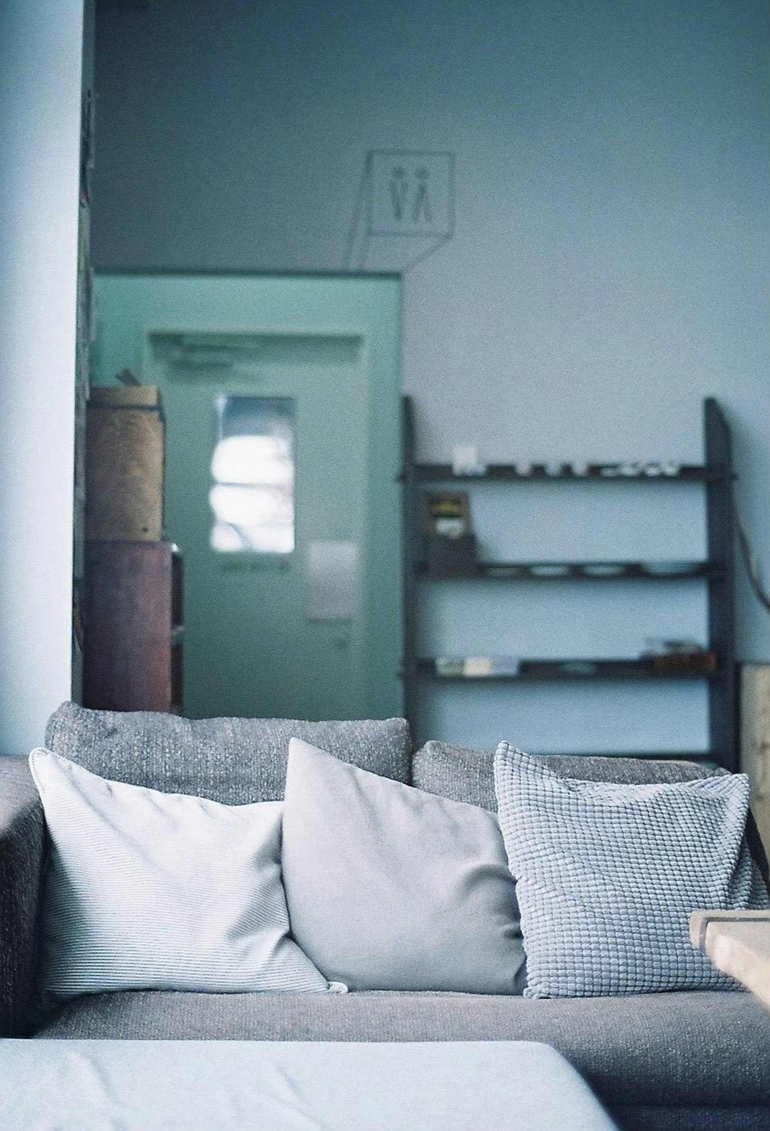 Foto von einem grauen Sofa mit Kissen in einem Raum mit blauen Wänden und einem Regal sowie einer Tür im Hintergrund