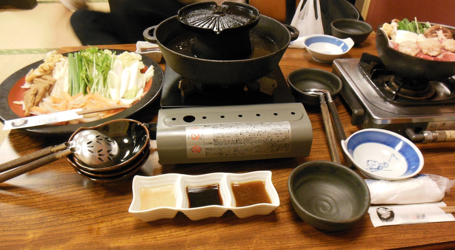 Table set with hot pot ingredients including vegetables and meat alongside sauces