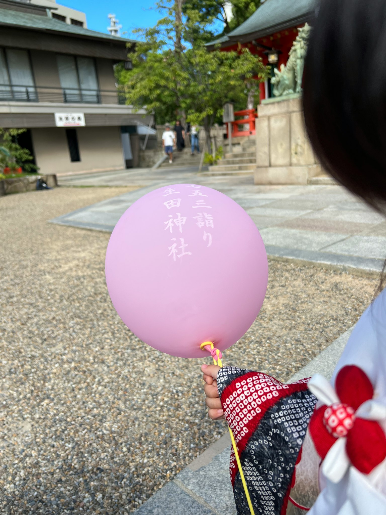 Anak memegang balon ungu dengan pakaian tradisional dan kuil di latar belakang