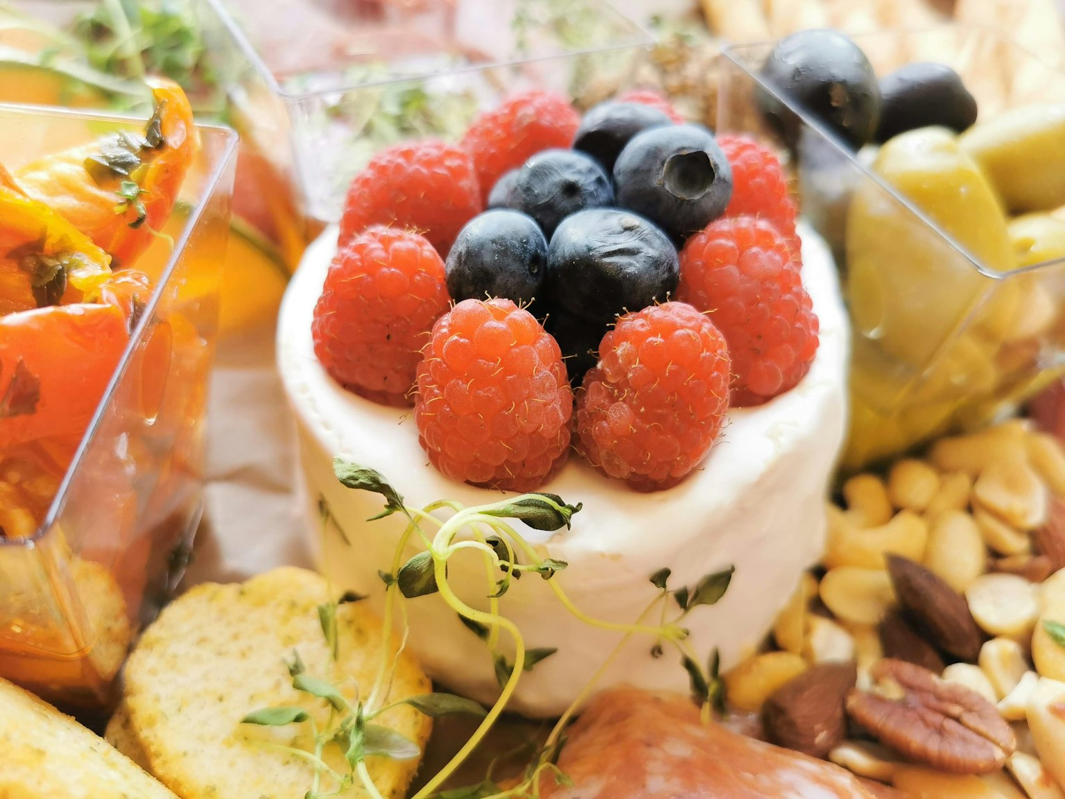Close-up of a dessert topped with raspberries and blueberries surrounded by assorted nuts