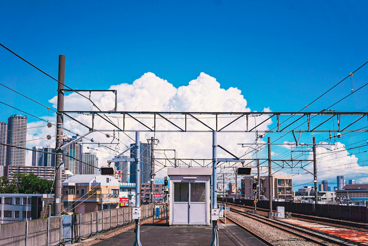 Vista della stazione con cielo blu e nuvole bianche che presenta binari e edifici