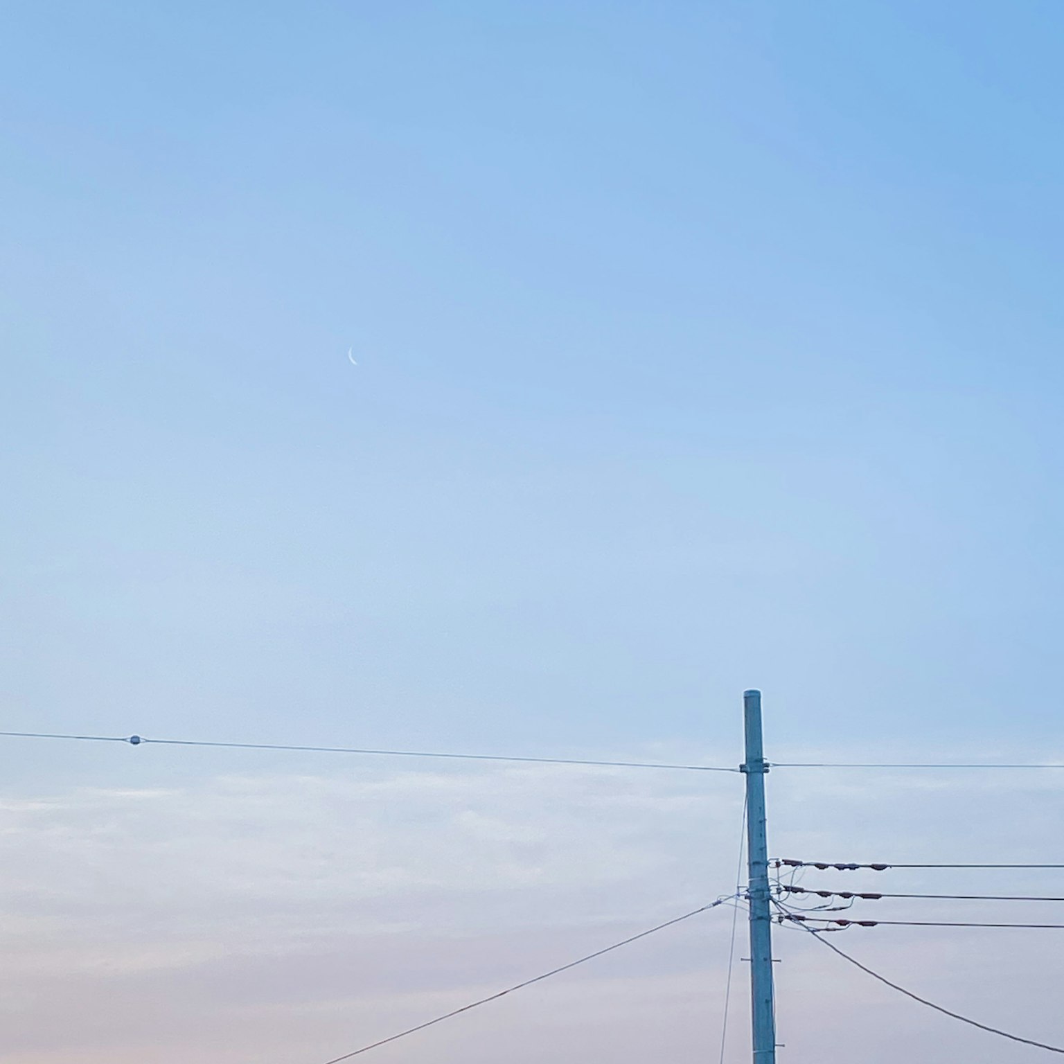 A utility pole and power lines against a blue sky with soft clouds