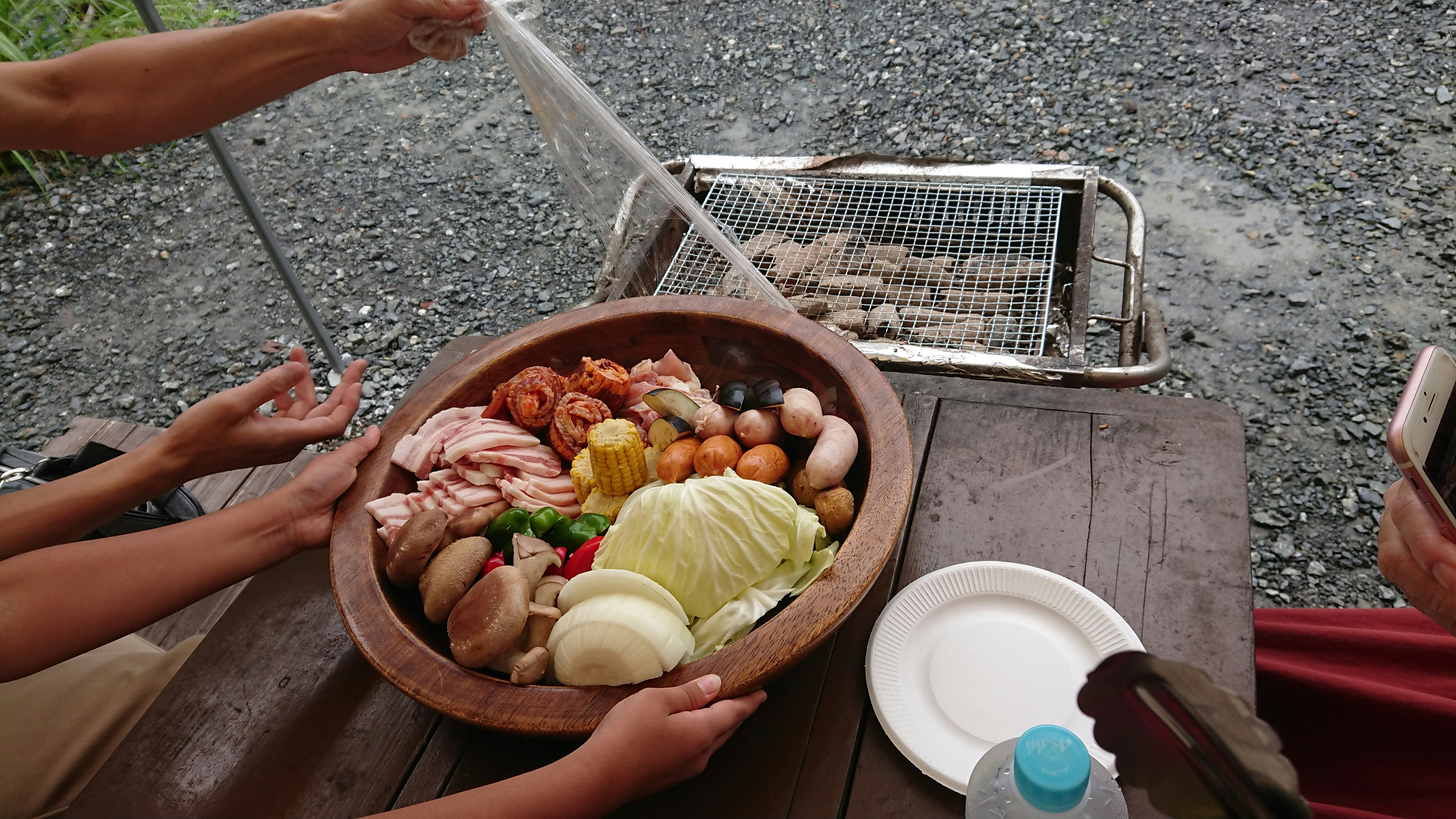 preparación de barbacoa al aire libre, manos colocando ingredientes en un cuenco