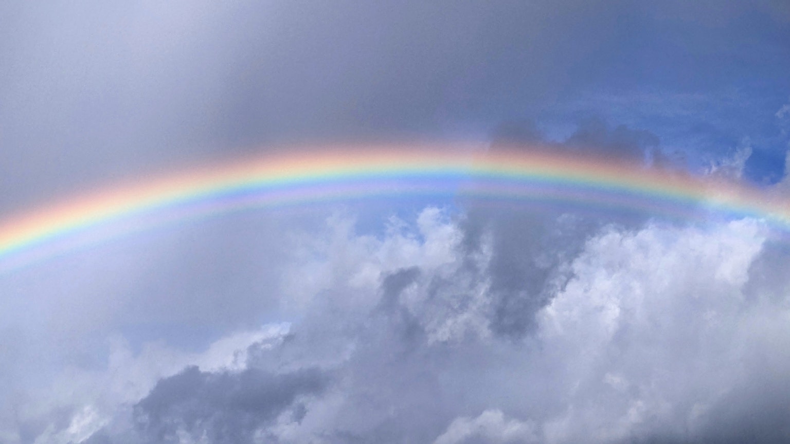 Un vivace arcobaleno che attraversa un cielo blu con nuvole soffici