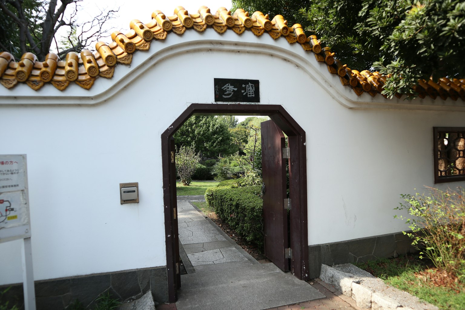 Traditionelles Tor mit weißen Wänden und goldenem Dach in einem ruhigen Garten