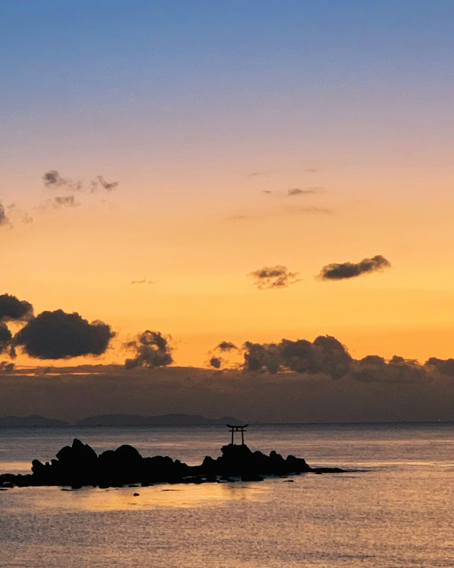 Hermoso atardecer sobre el océano con una cruz en las rocas y cielo naranja