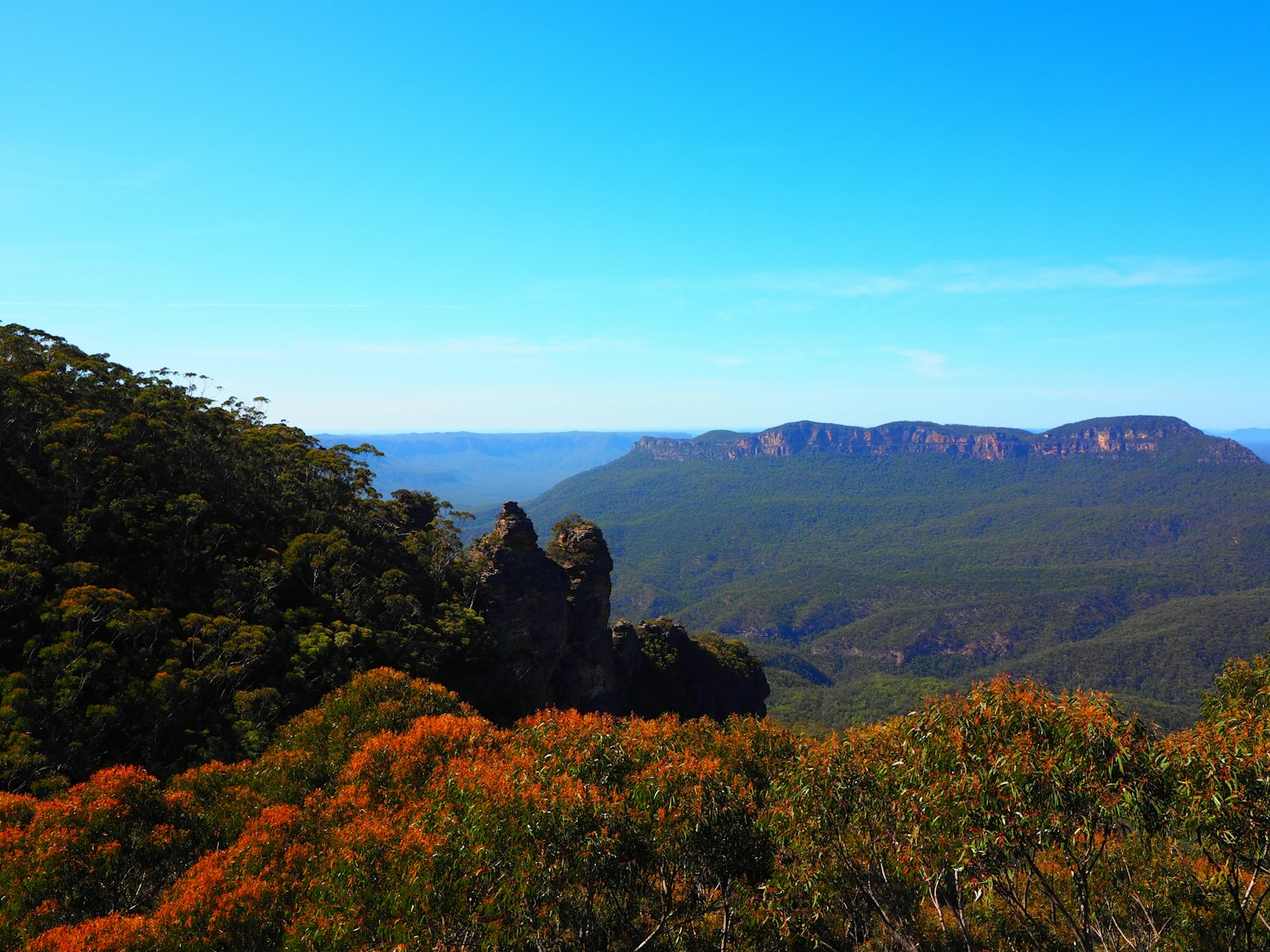 Vista escénica de montañas verdes y follaje naranja bajo un cielo azul