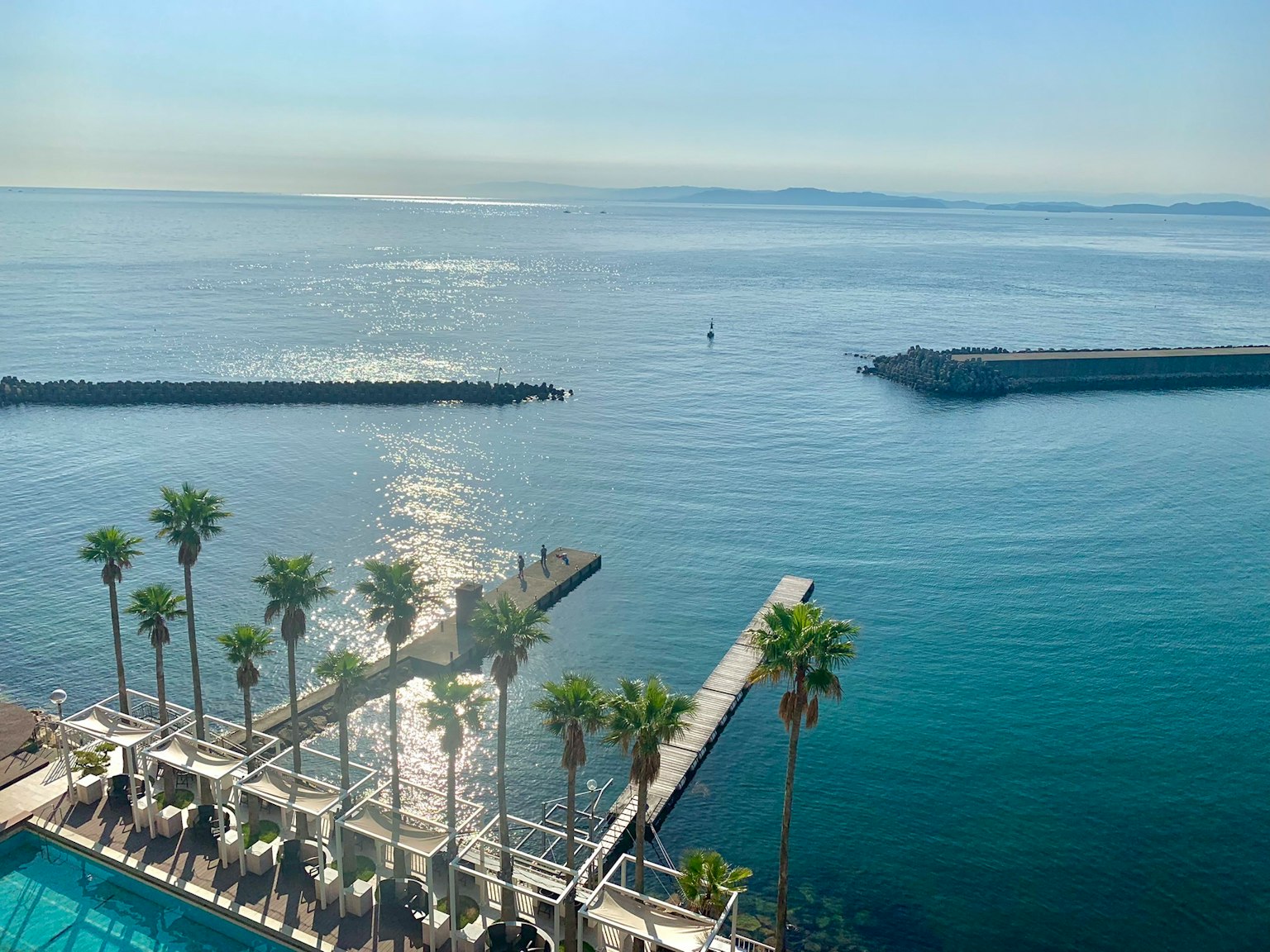 Resort scene with palm trees and a pier against a blue ocean and sky