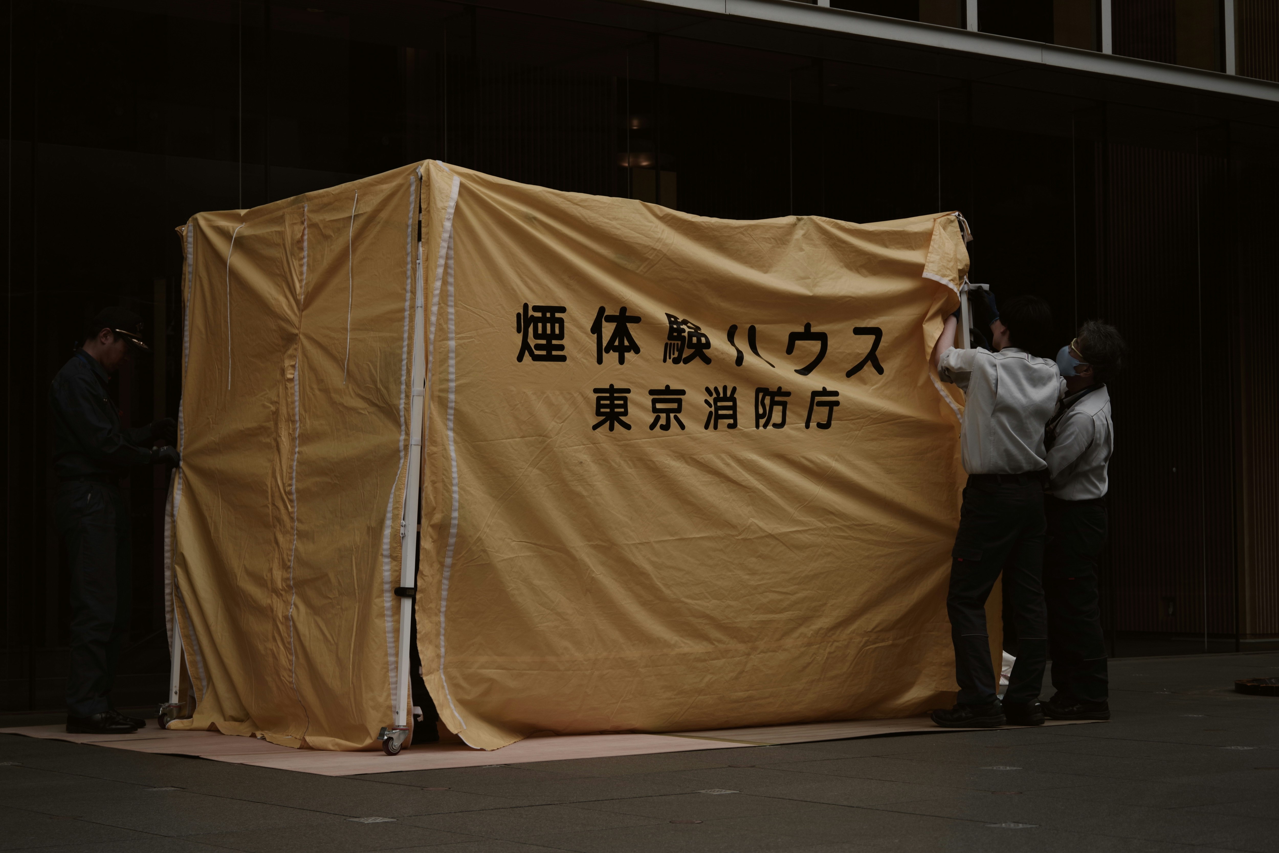 黄色い「ハウス」型の仮設テントと煙のある東京の街並み
