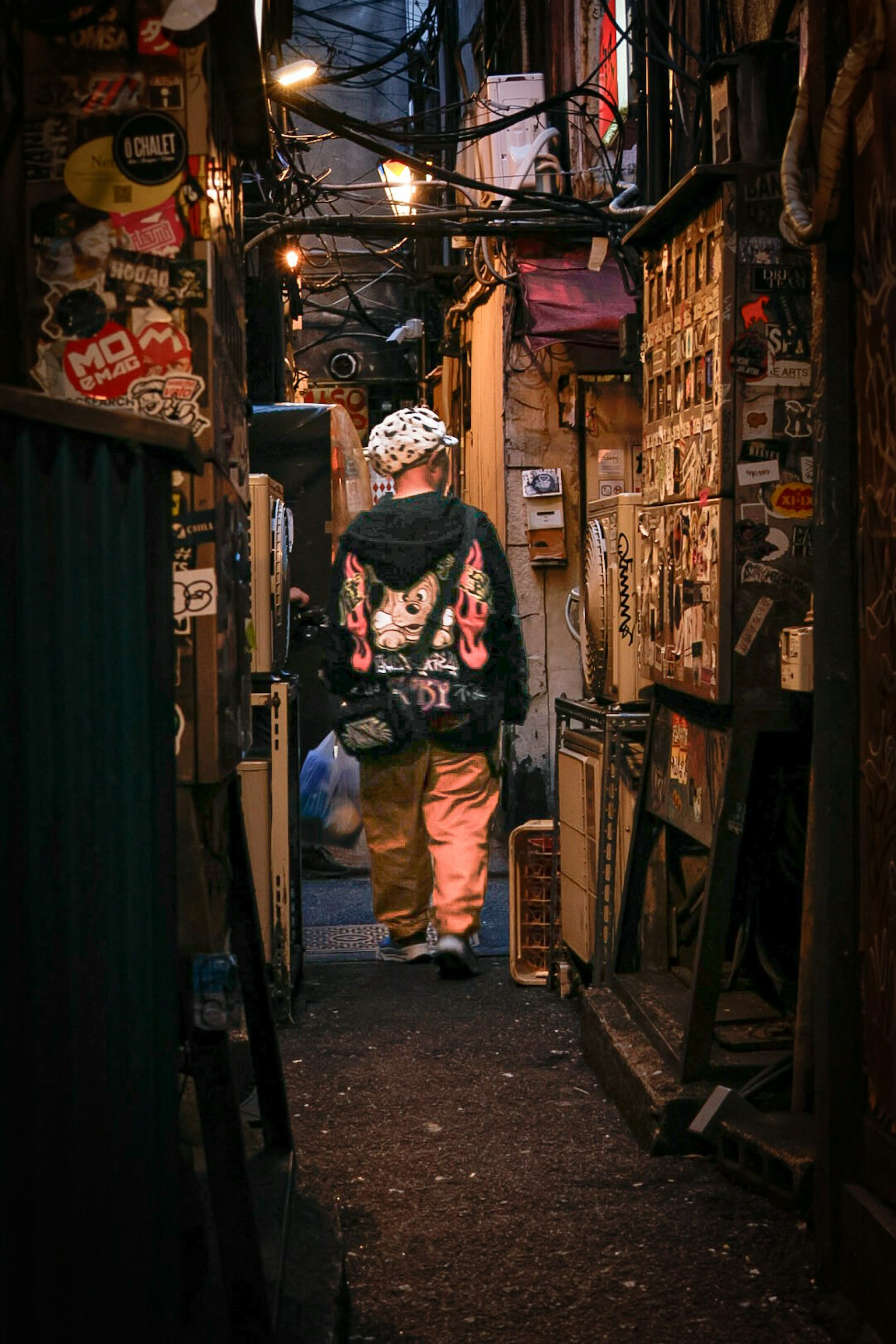 狭い路地を歩く人物と壁に貼られたステッカーが特徴的な風景