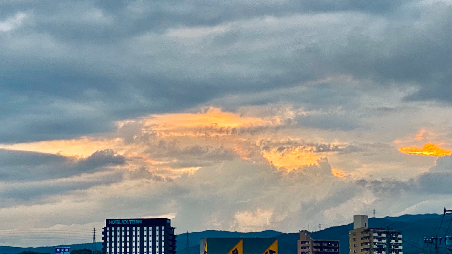 曇り空に浮かぶオレンジ色の雲と建物のシルエット