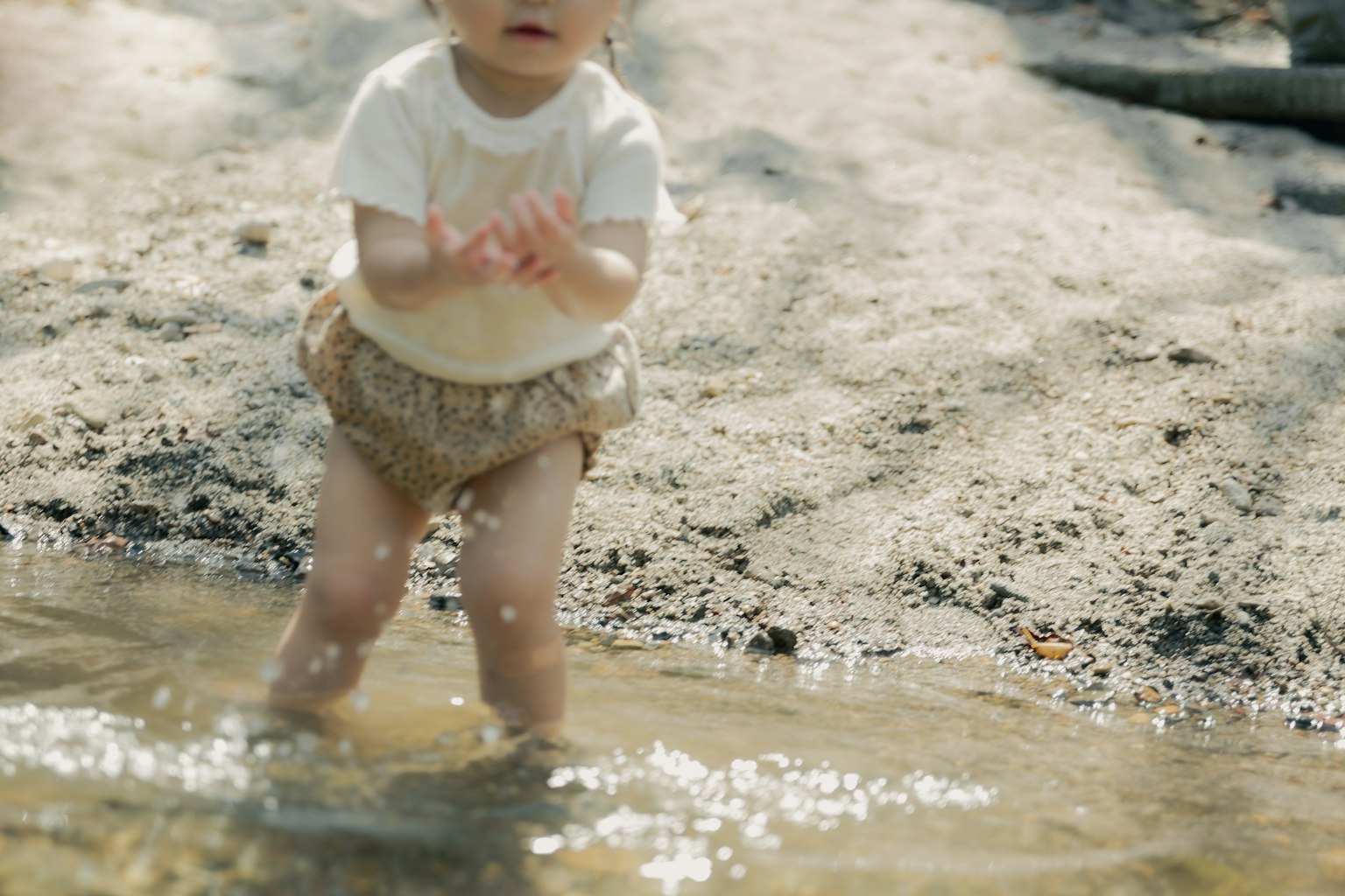 Enfant jouant dans une flaque d'eau portant un short beige et un t-shirt blanc