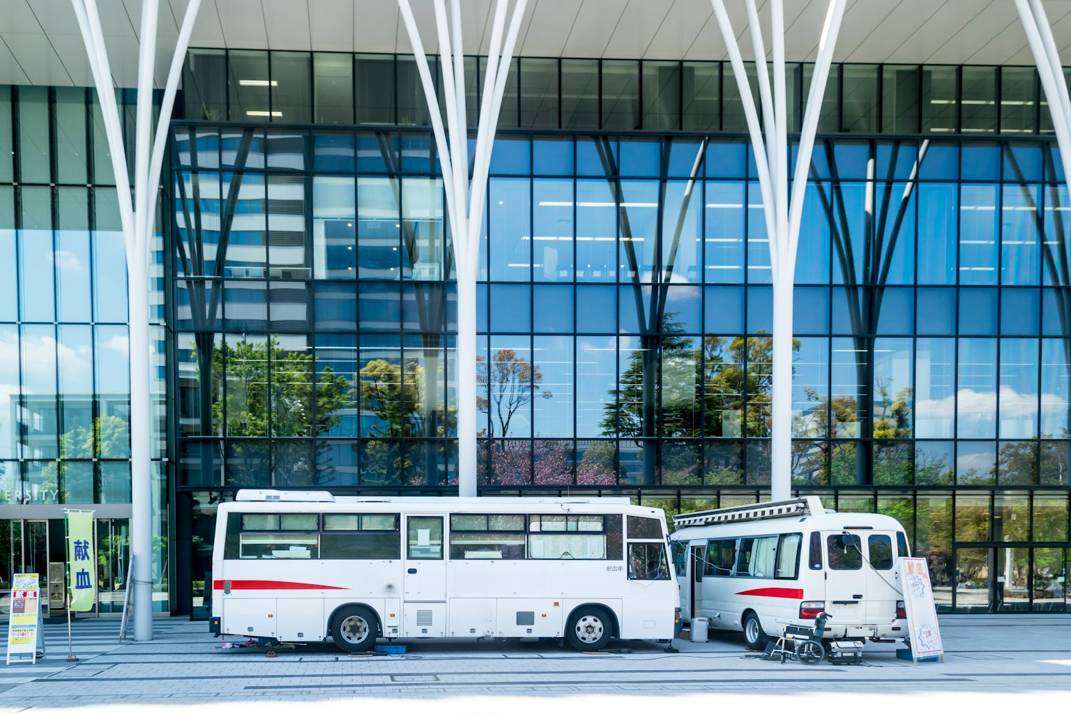 Autobús y furgón blancos estacionados frente a un edificio moderno de vidrio