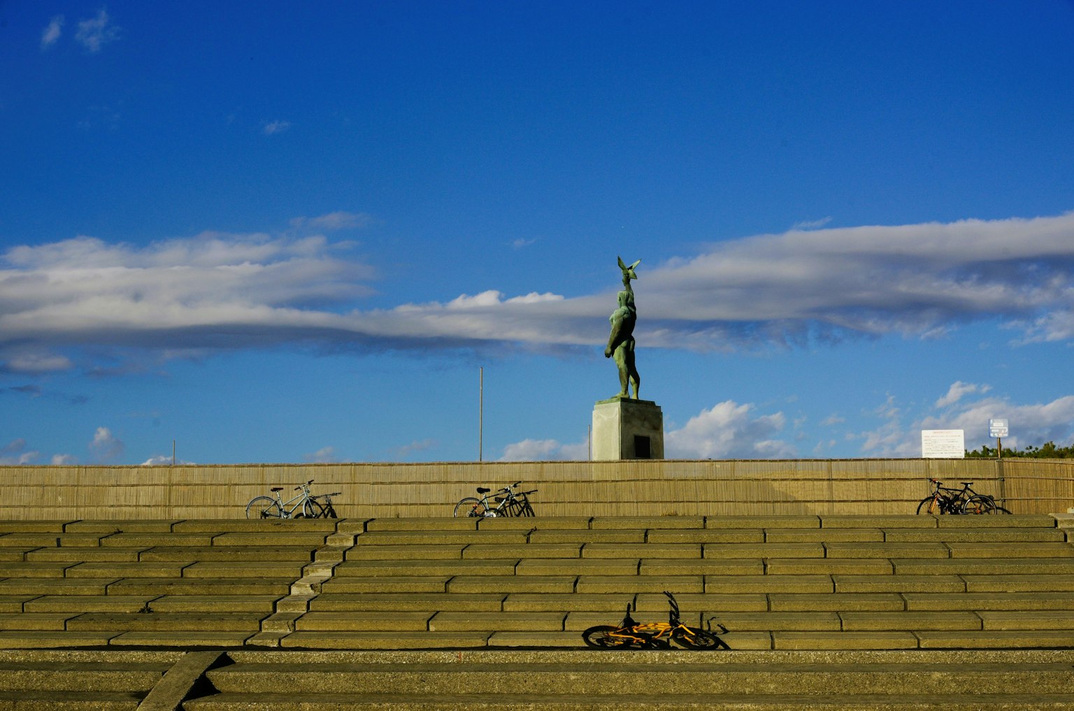 Grüne Statue steht unter einem blauen Himmel mit Steinstufen