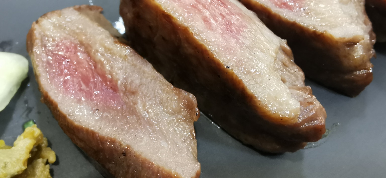 Viande tranchée montrant le contraste entre le rouge et la graisse sur une assiette noire avec du wasabi et de la sauce sur le côté