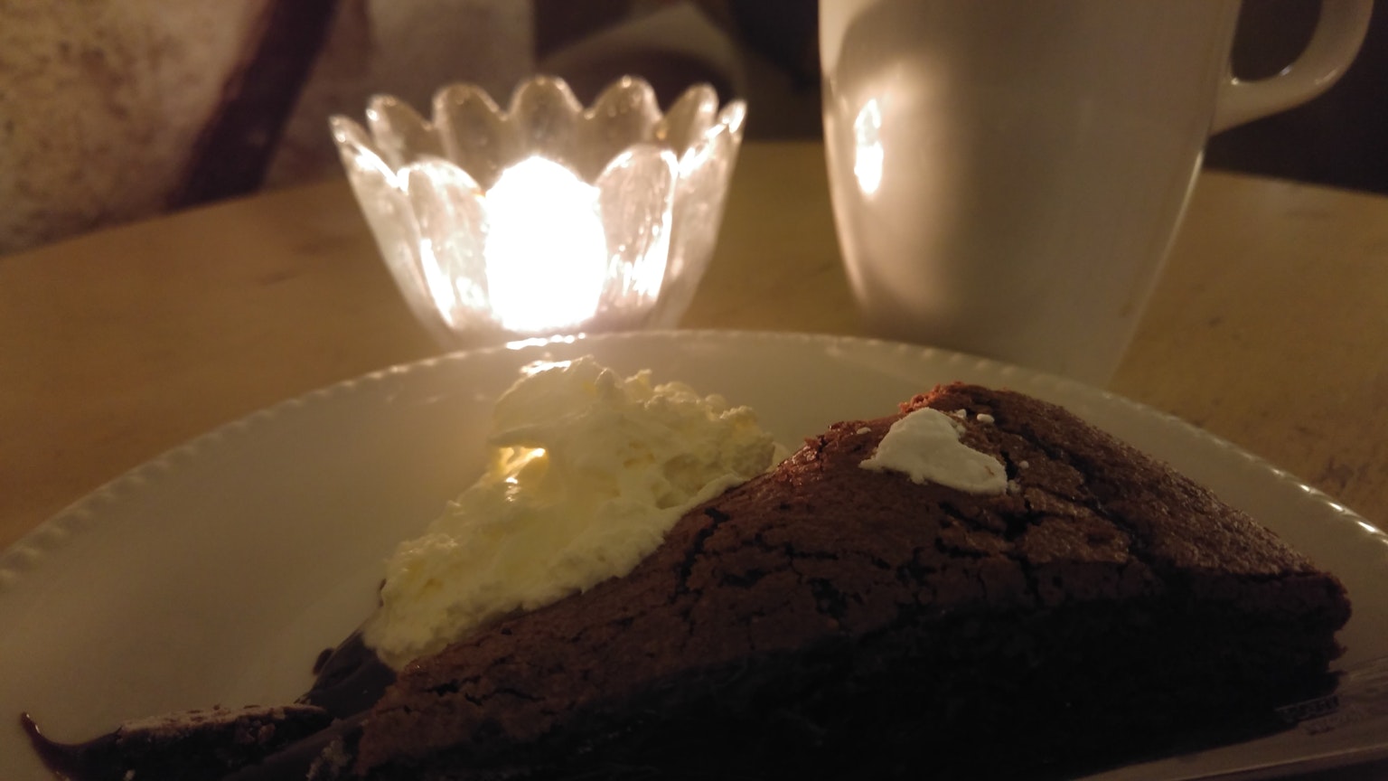 Part de gâteau au chocolat avec de la crème fouettée à côté d'une bougie et d'une tasse de café