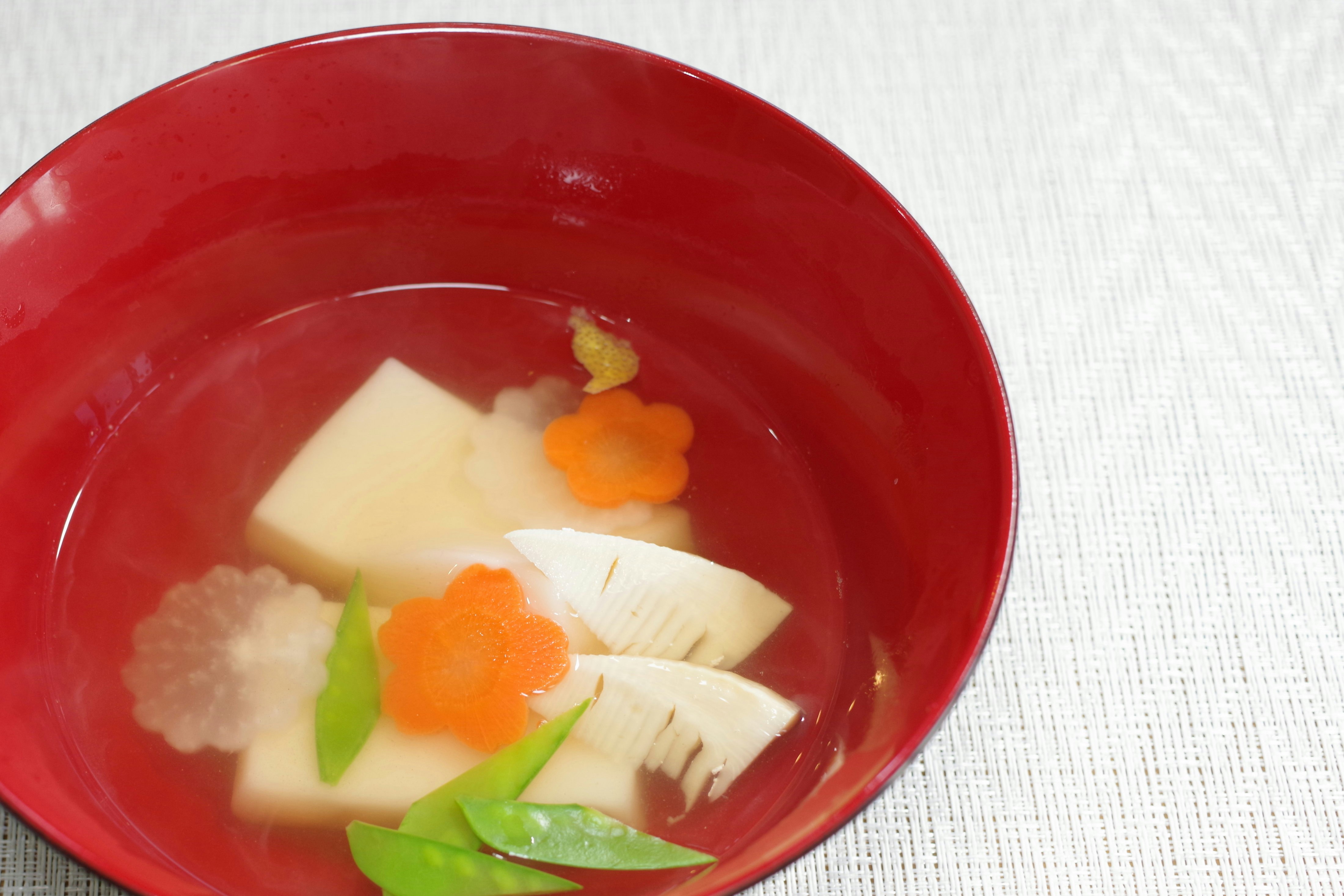 赤い器の味噌汁に入った大根・にんじん・ねぎ