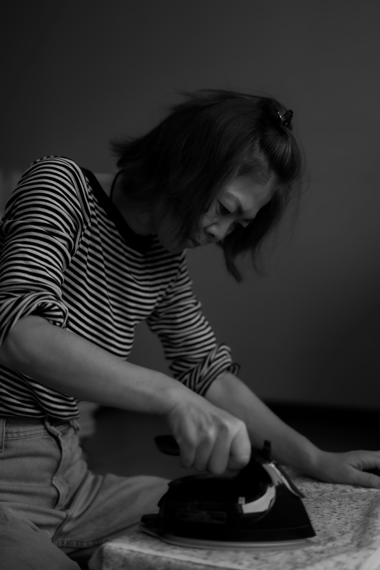 Eine Frau in einem gestreiften Hemd, die Kleidung in einem Schwarz-Weiß-Bild bügelt