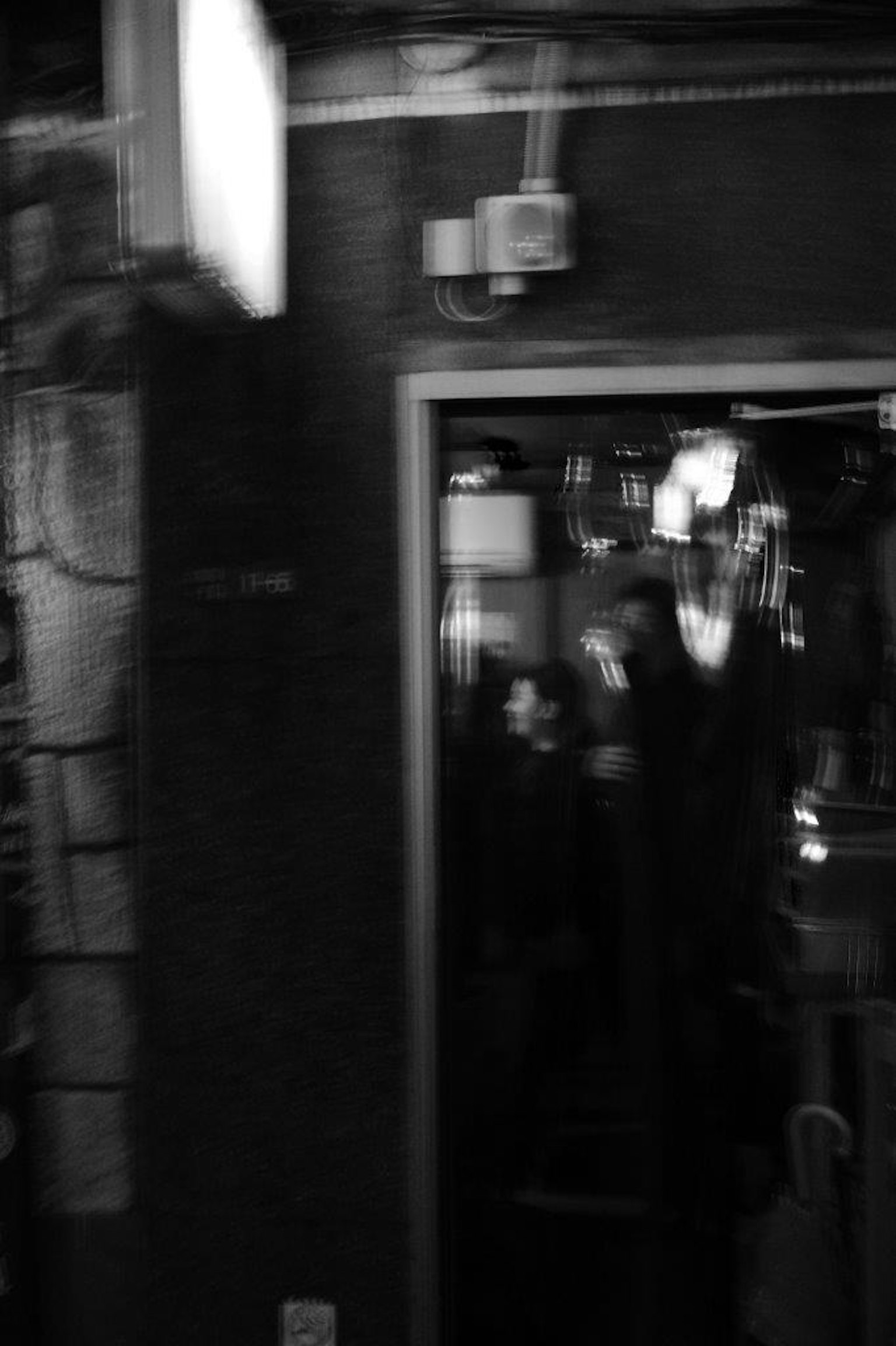 Image en noir et blanc montrant une porte avec une silhouette dans l'ombre à l'intérieur