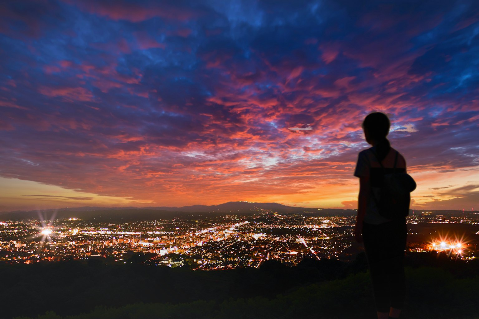Silhouette eines Jungen, der vor einem Sonnenuntergangshimmel mit Stadtlichtern steht