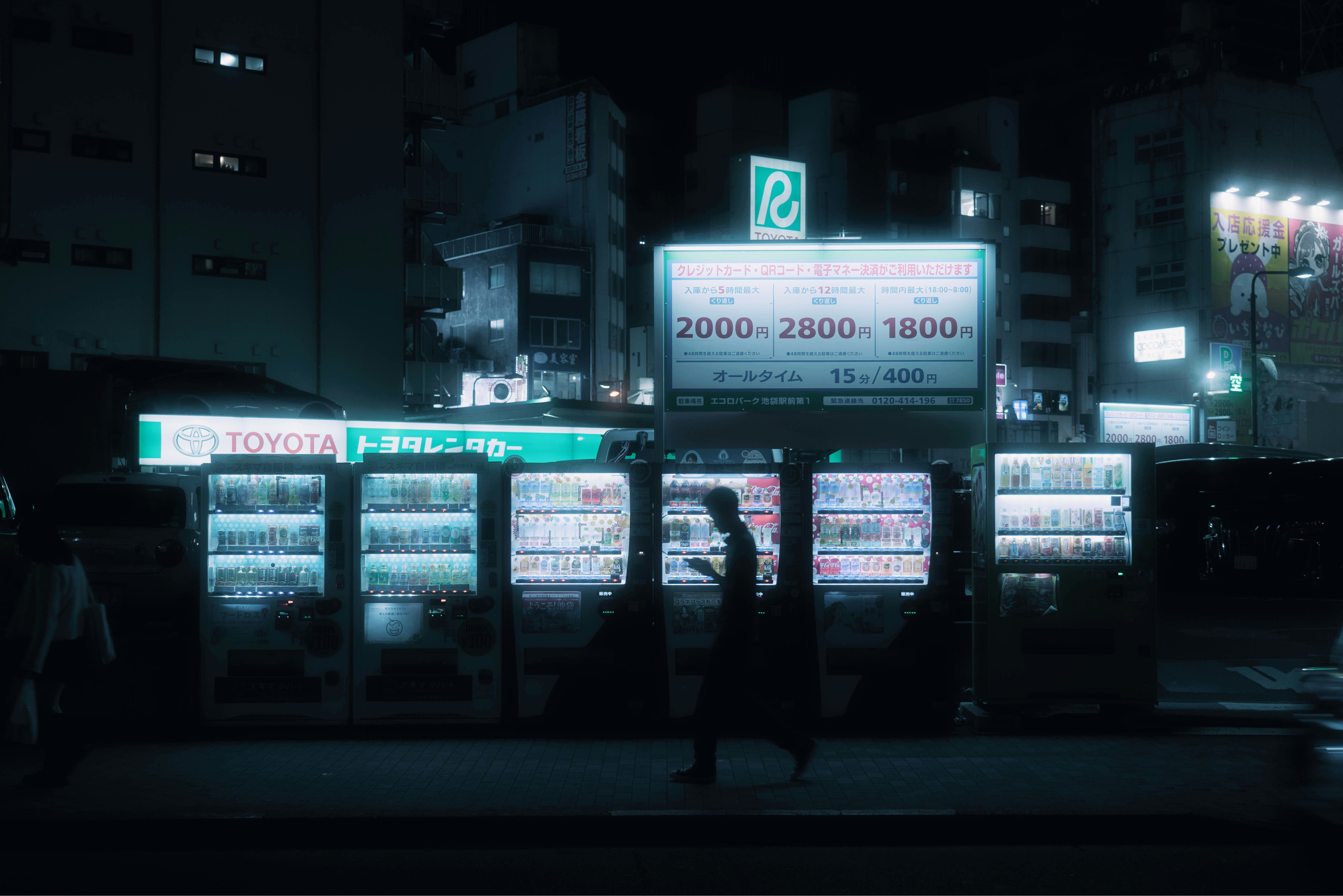 夜の街角に並ぶ自動販売機と看板のある通り