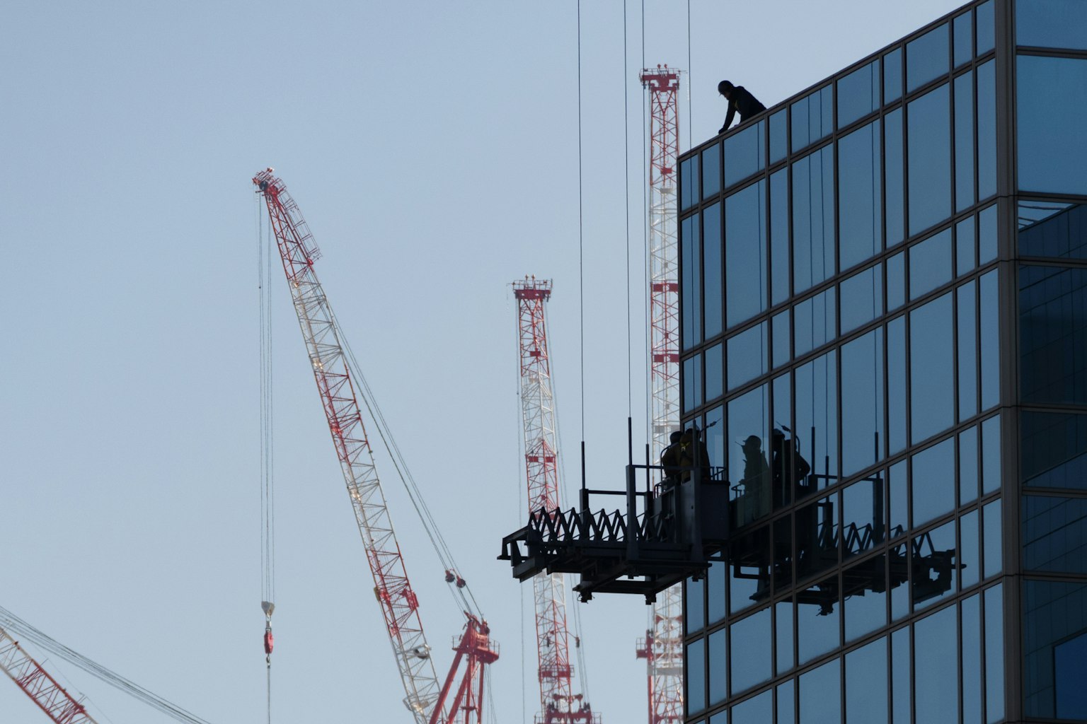 Pekerja membersihkan jendela gedung pencakar langit dengan crane di latar belakang