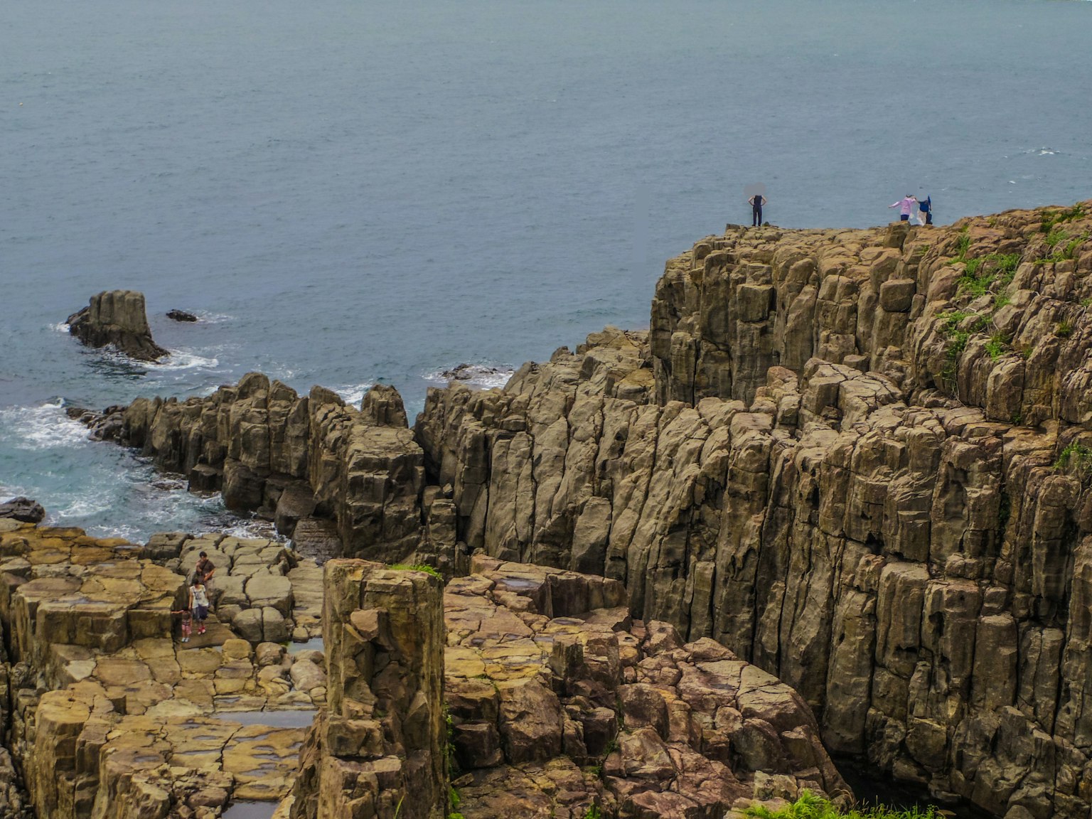 Persone in piedi su una costa rocciosa che guarda il mare calmo