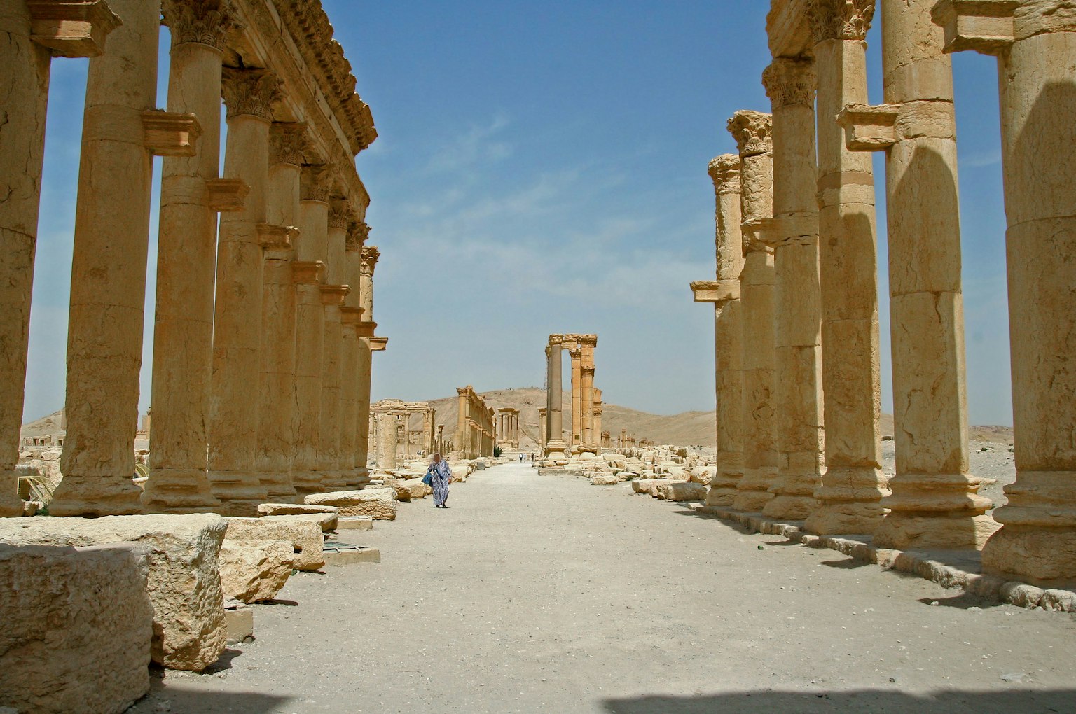 Pathway lined with ancient columns under a clear blue sky