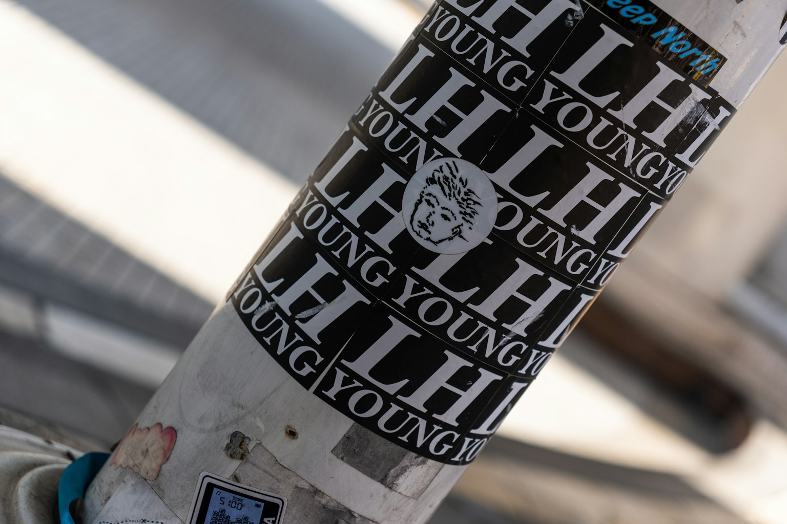 一根覆蓋著黑白貼紙的柱子，上面重複印刷著'YOUNG'和'LH'的文字