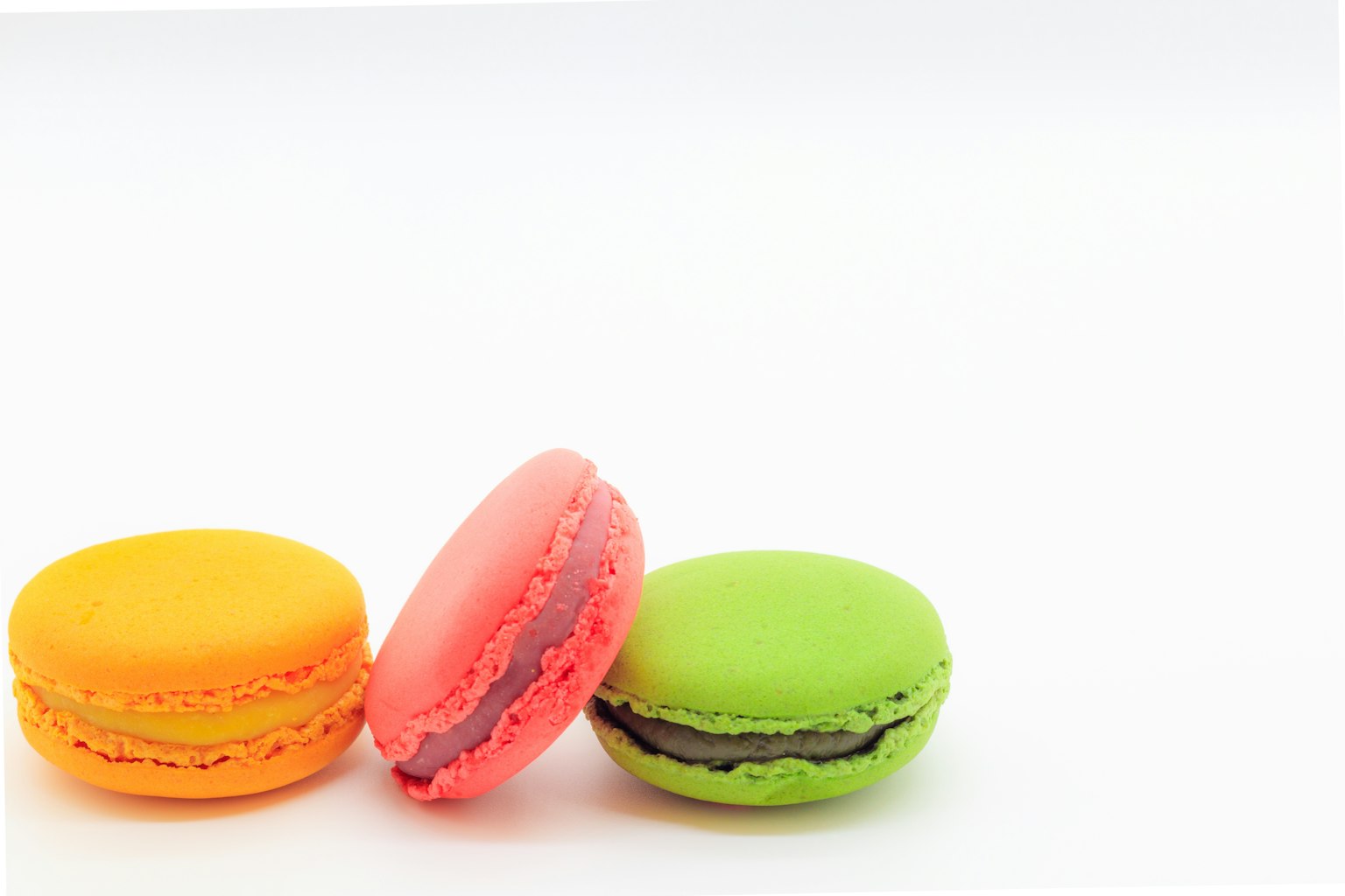 Colorful macarons in orange, pink, and green on a white background