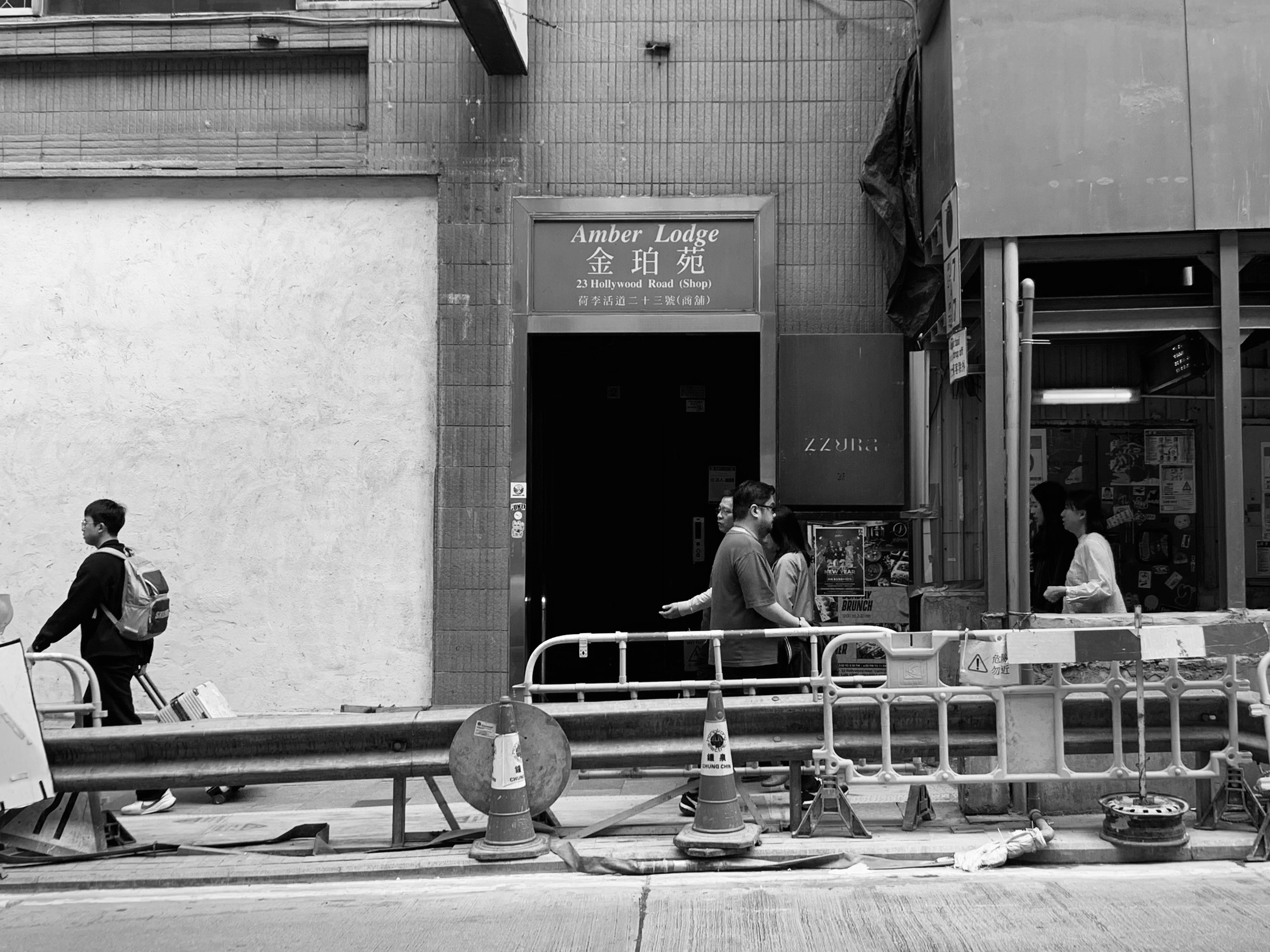 人々が通りを歩くモノクロの都市風景 工事中のバリケードと店舗の看板が見える