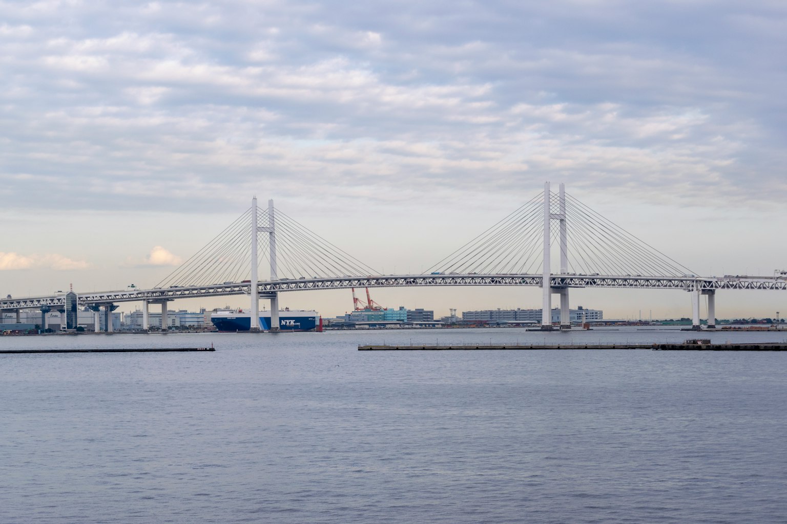 Jembatan Teluk Yokohama membentang di atas air dengan kapal biru dan awan di latar belakang