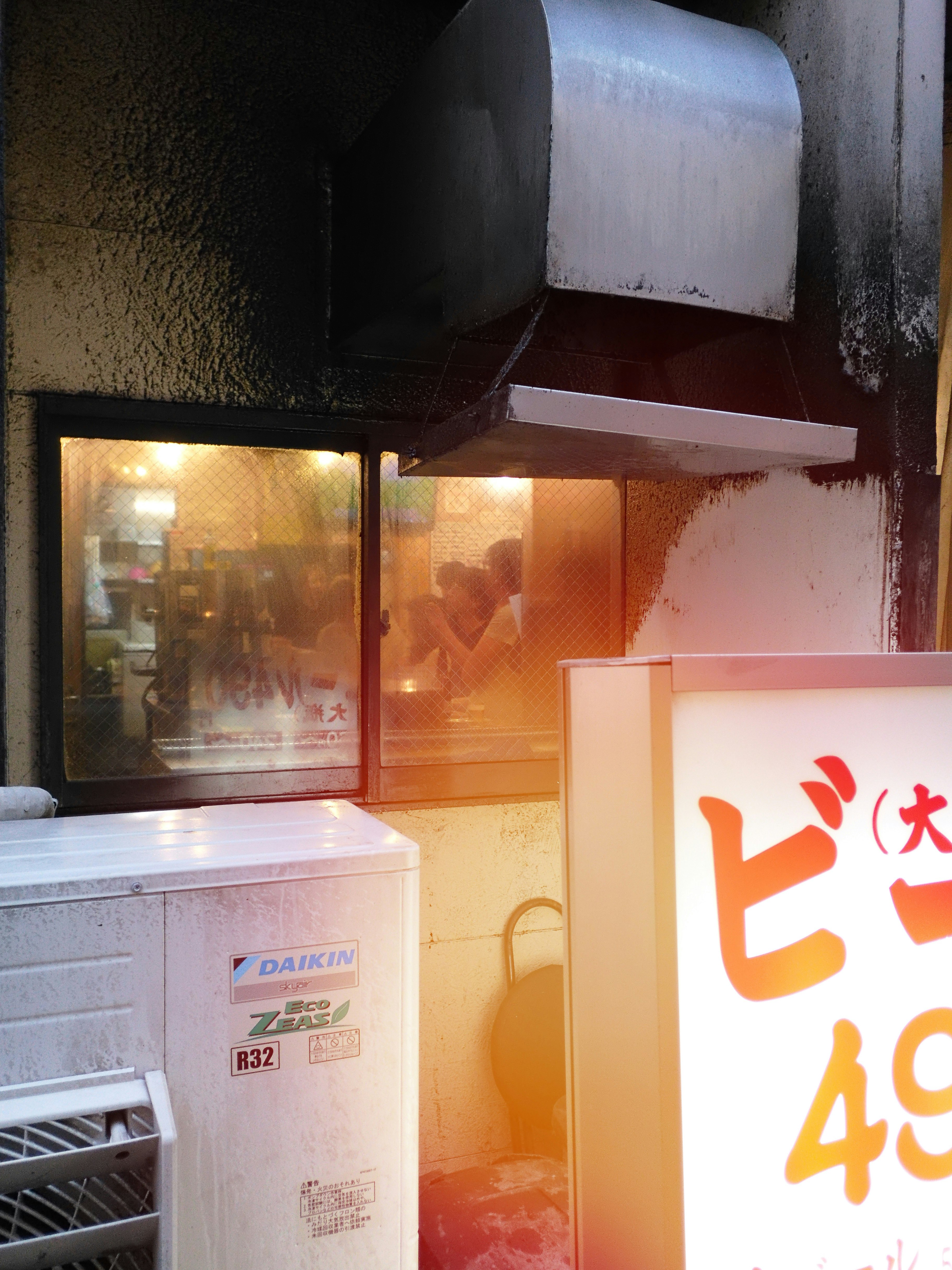 路地の店先に並ぶ看板と商品ケースのある小さな屋外スペース