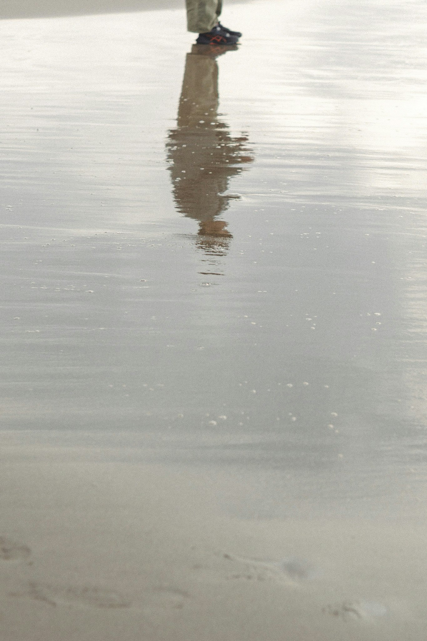 水面に映る足元と波紋のある砂浜
