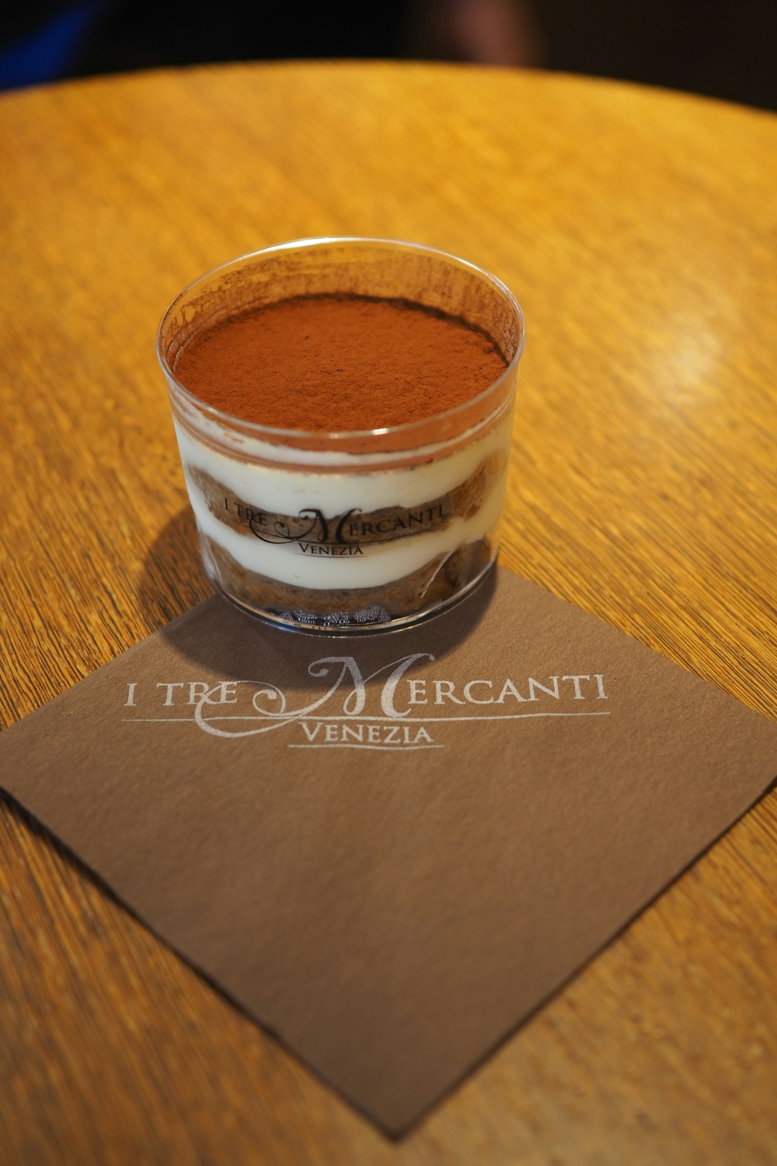 Clear cup with tiramisu on a wooden table with a branded napkin